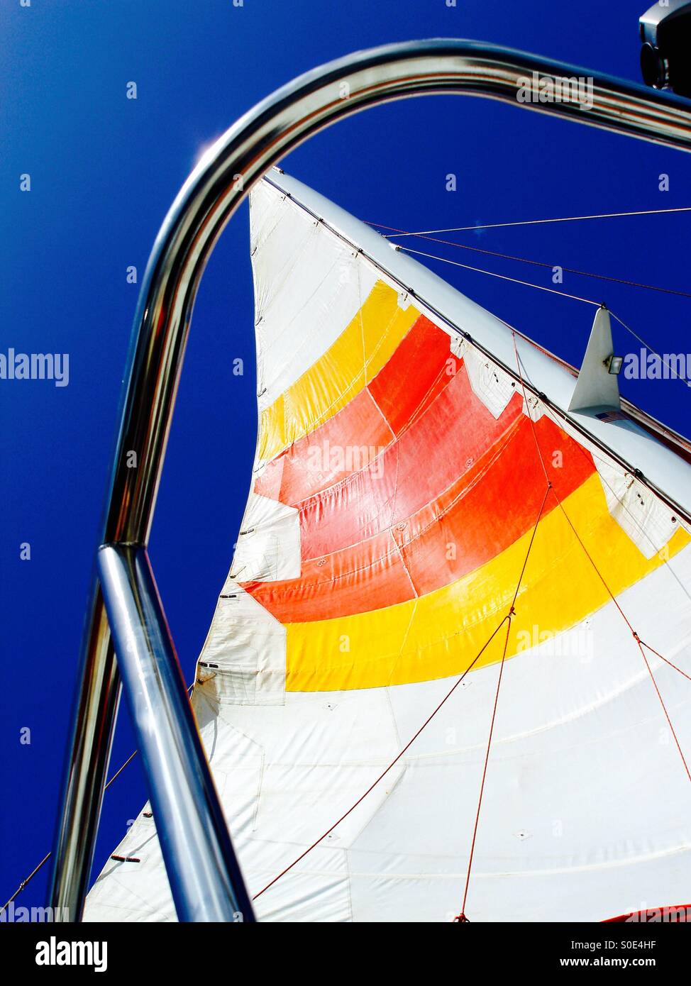 Colorful ship's sails in red, yellow and white pop against an azure blue sky - Smartphone Captured Stock Image