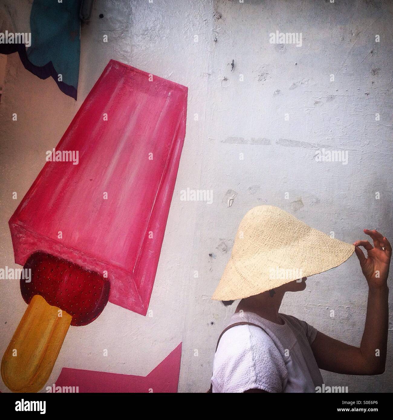 A woman holds a straw hat as she poses near a painting of a Michoacana ice cream shop in Condesa, Mexico City, Mexico Stock Photo