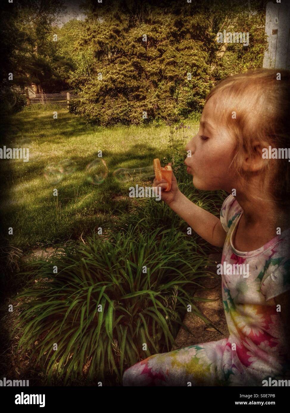 A girl in a floral dress sits on a patio blowing bubbles (3). - Smartphone Captured Stock Image