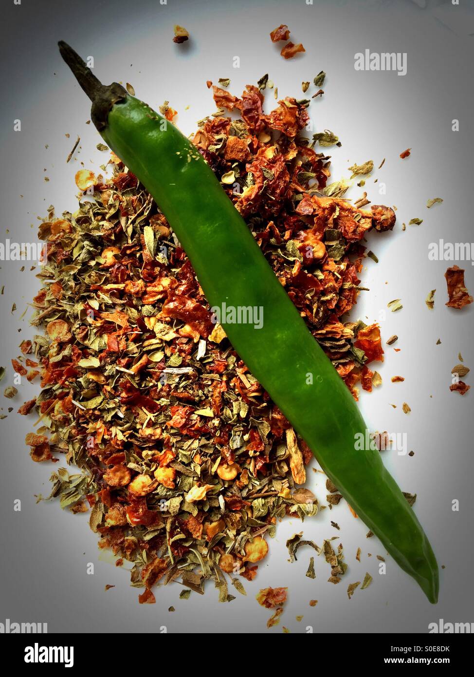 A green chilli on a bed of chilli flakes and oregano Stock Photo Alamy
