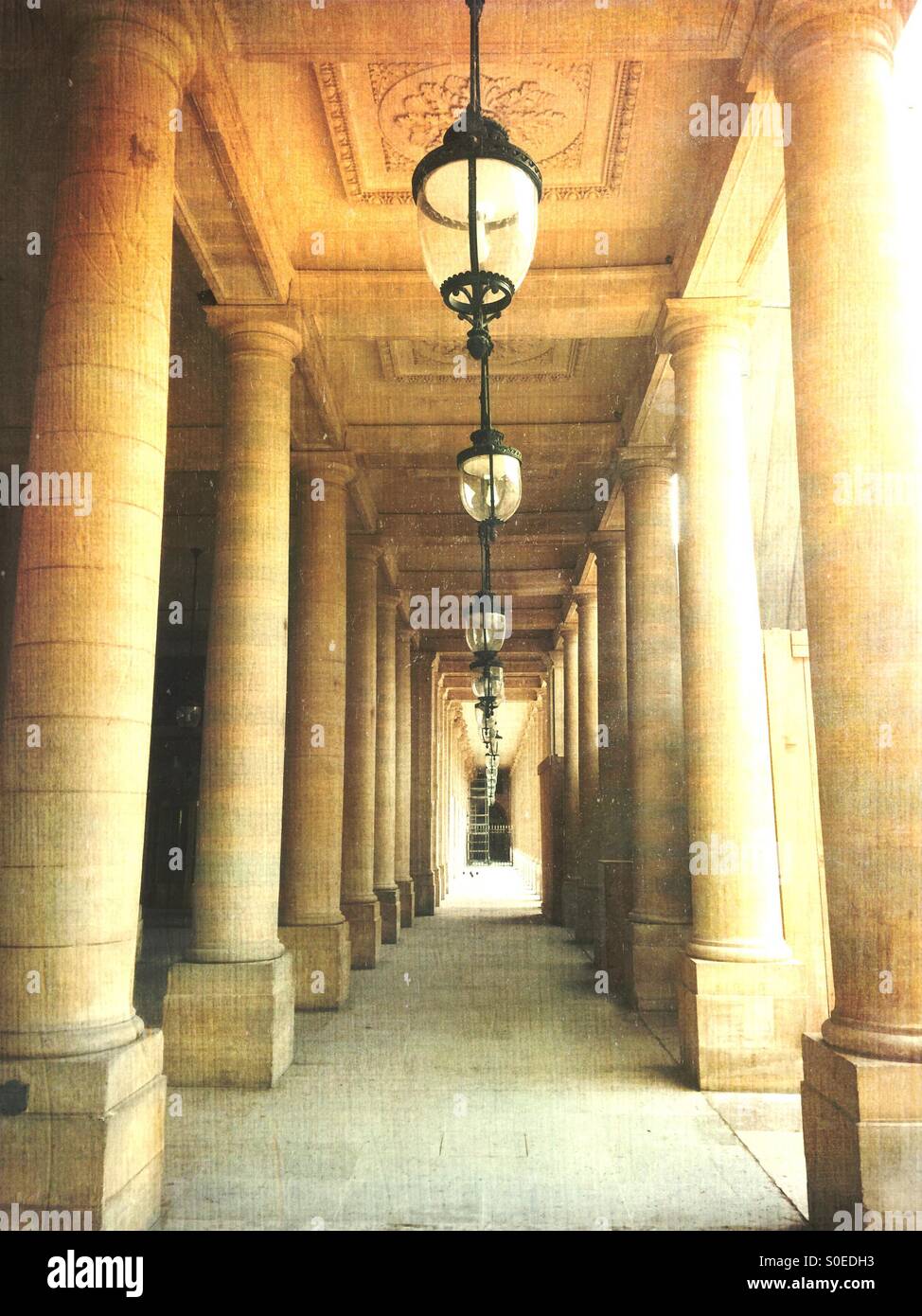 Beautiful classical columns and antique pendant ceiling lamps line the arcade of Valois Gallery at Palais-Royal. 1st arrondissement or district in central Paris, France. Vintage texture overlay. Stock Photo