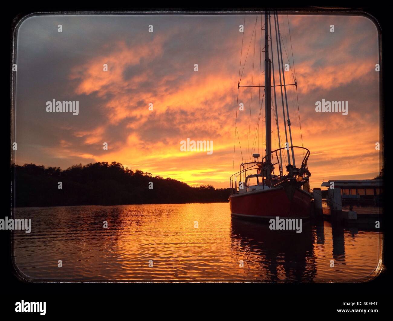 Sailboat in front of orange sunrise in Woy Woy creek Stock Photo