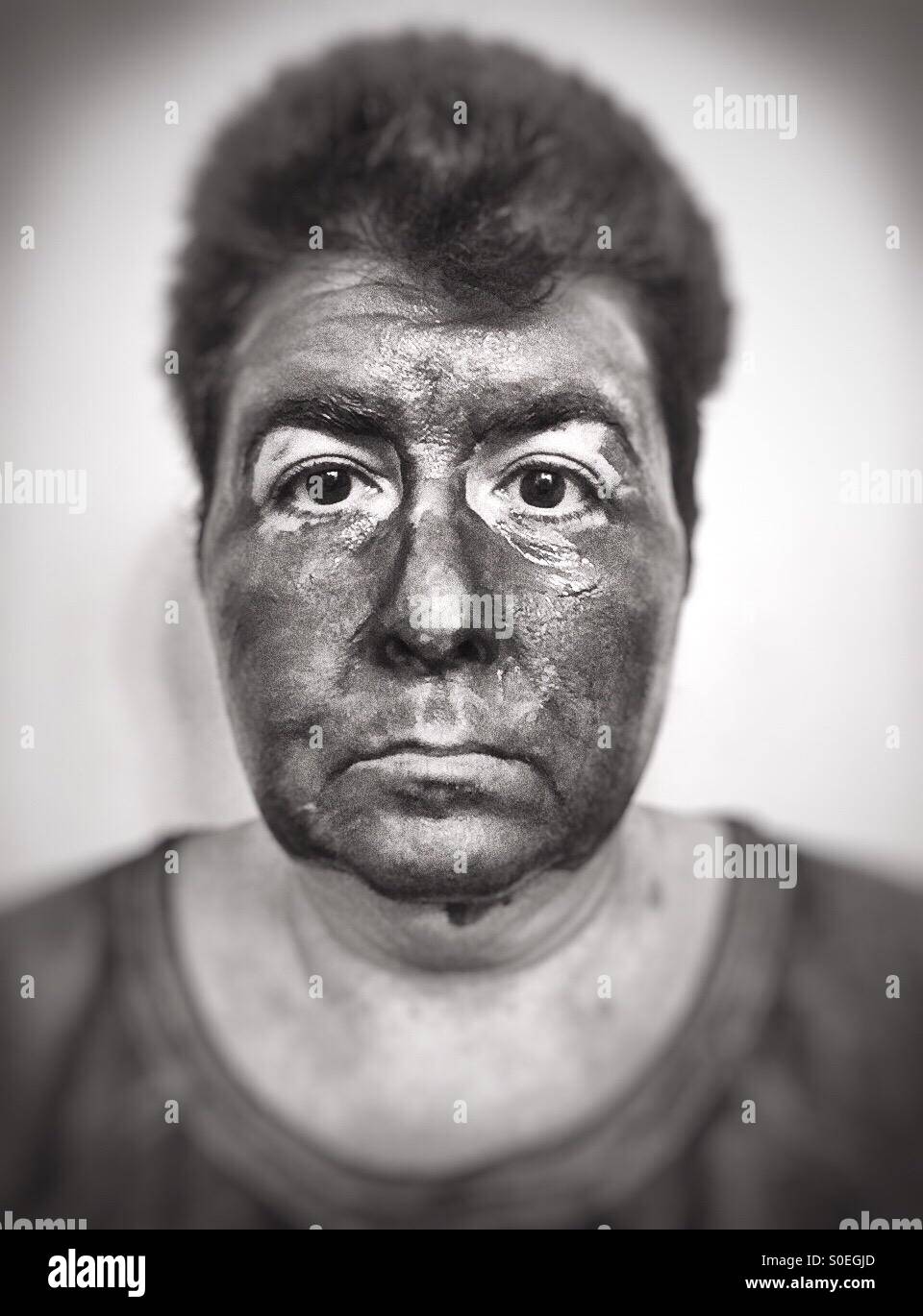 A woman with a mud mask on poses like a mug shot - black and white Stock Photo