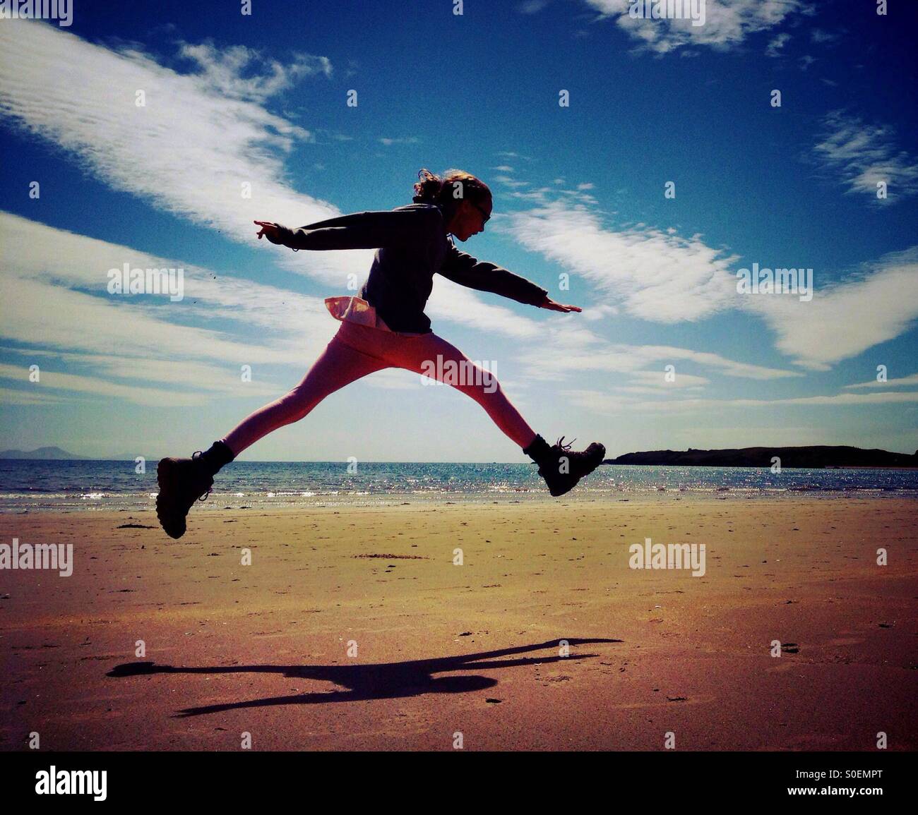 Young girl leaping for joy on Newborough beach on Anglesey Stock Photo