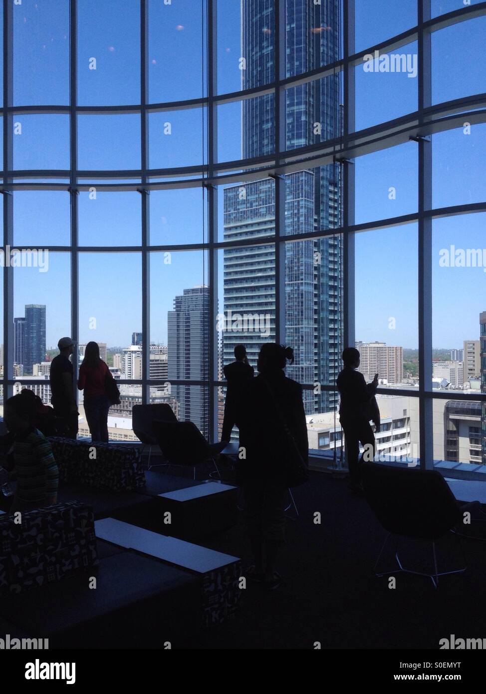 Silhouettes of people viewing a skyscraper through atrium glass panel Stock Photo