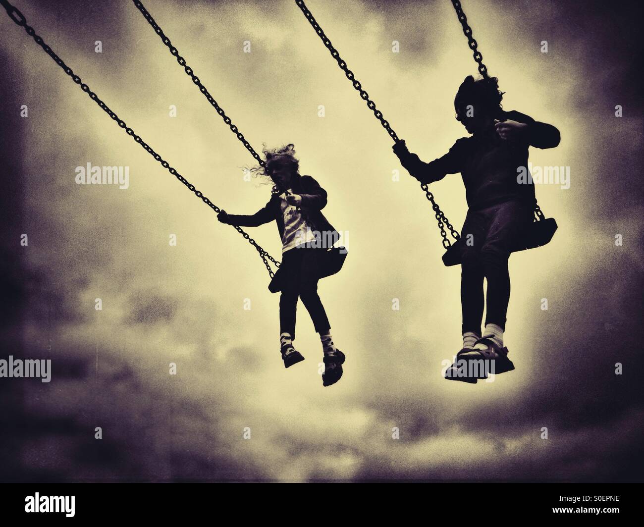 Two girls on swings in silhouette against cloudy sky Stock Photo Alamy