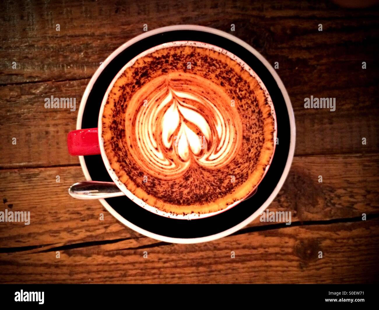 Cup of cappuccino coffee in a cafe on a wooden table viewed from above. Flower pattern in the frothy milk - Smartphone Captured Stock Image