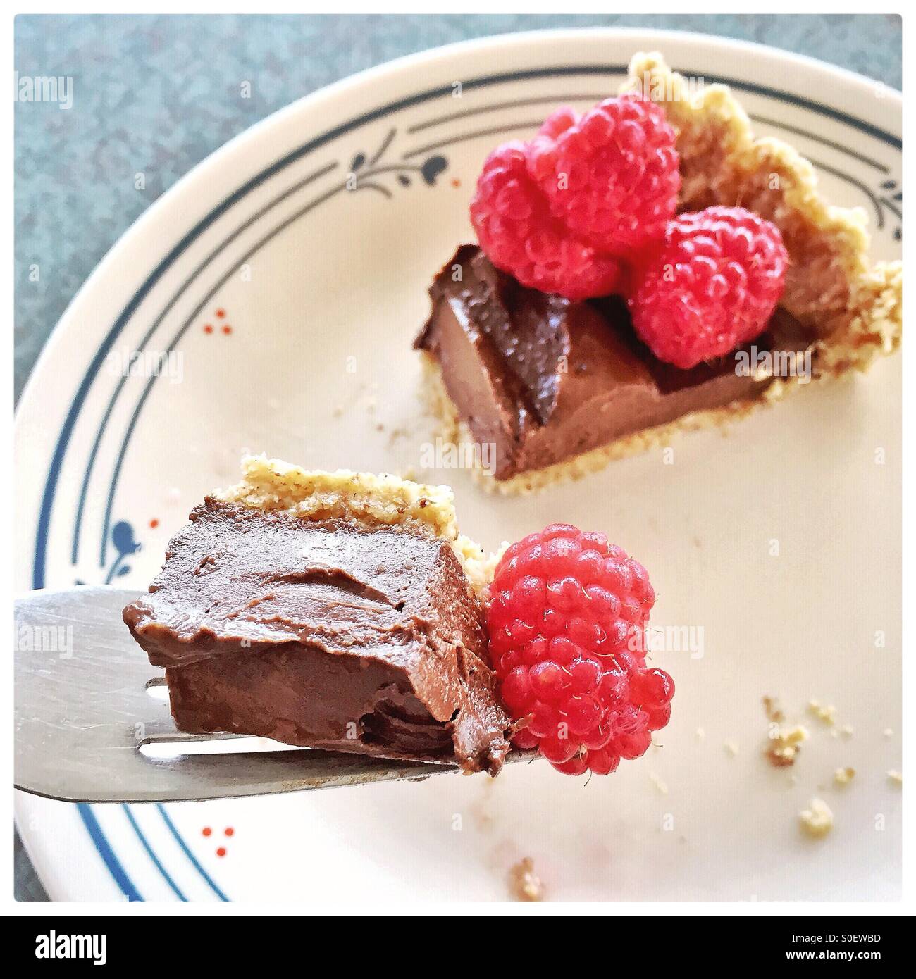A sliver of chocolate torte topped with raspberries is in the background with a bite on a fork in the foreground. Stock Photo