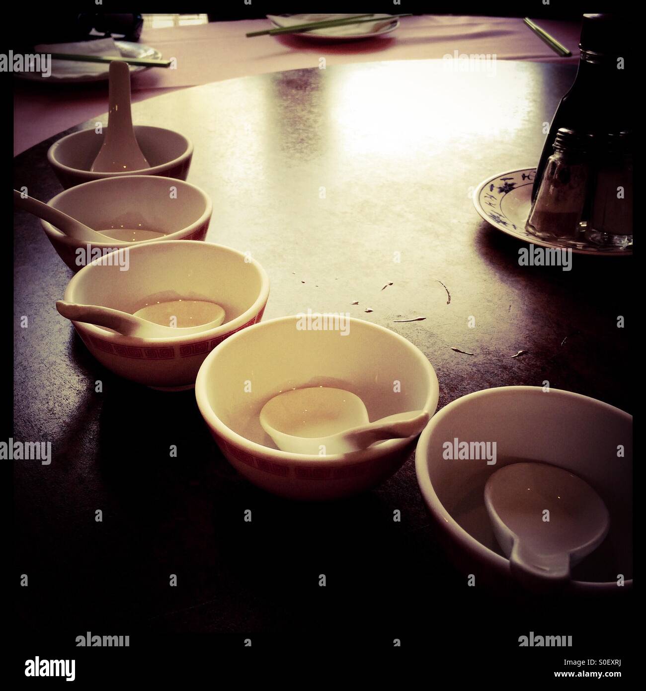 Empty Chinese bowls with spoons in them on a table. - Smartphone Captured Stock Image