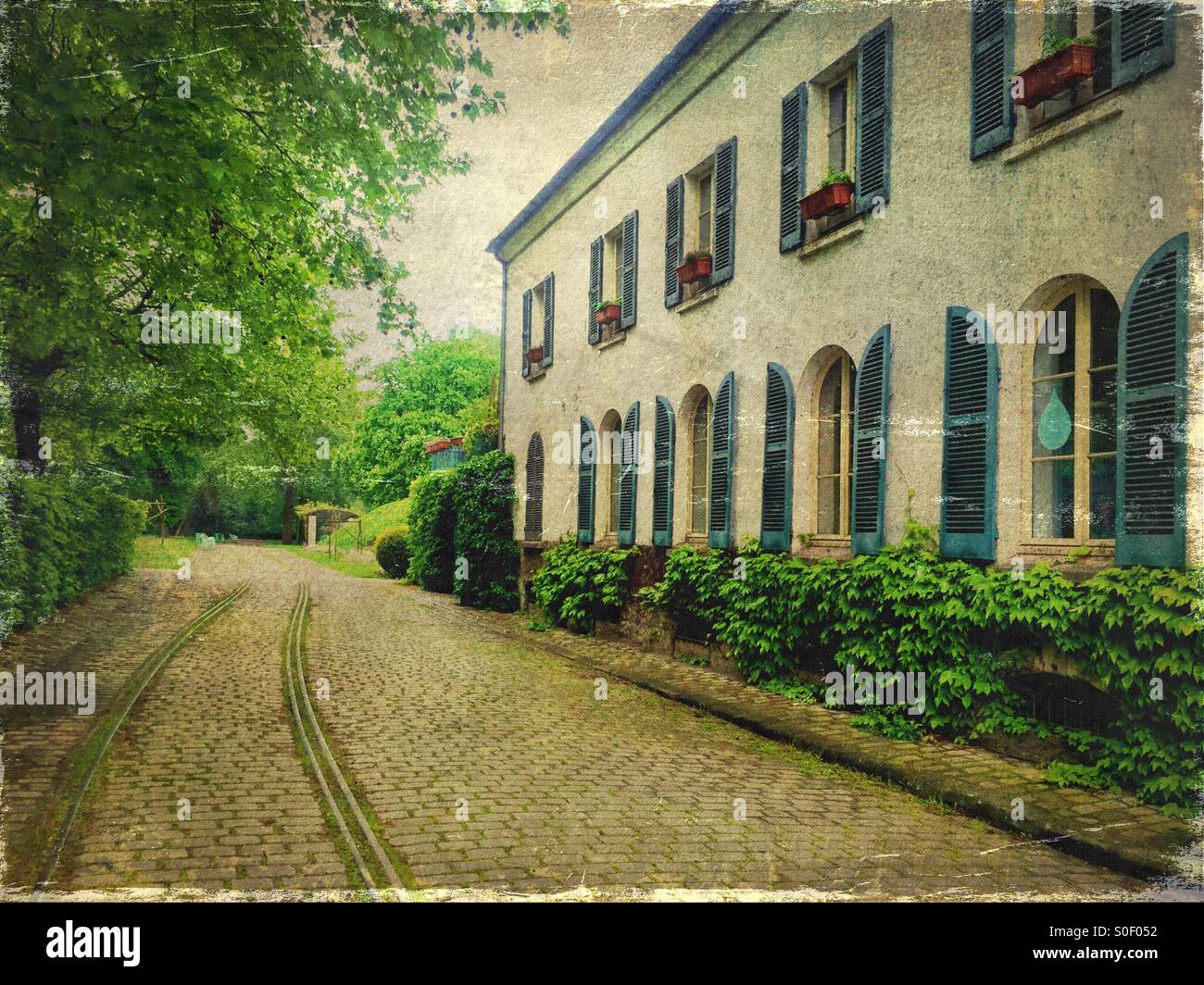 View of Maison du Jardinage with pretty blue shutters at Parc de Bercy in Paris, France. Brick pavement, trees and fresh Spring foliage with vintage texture overlay. Stock Photo