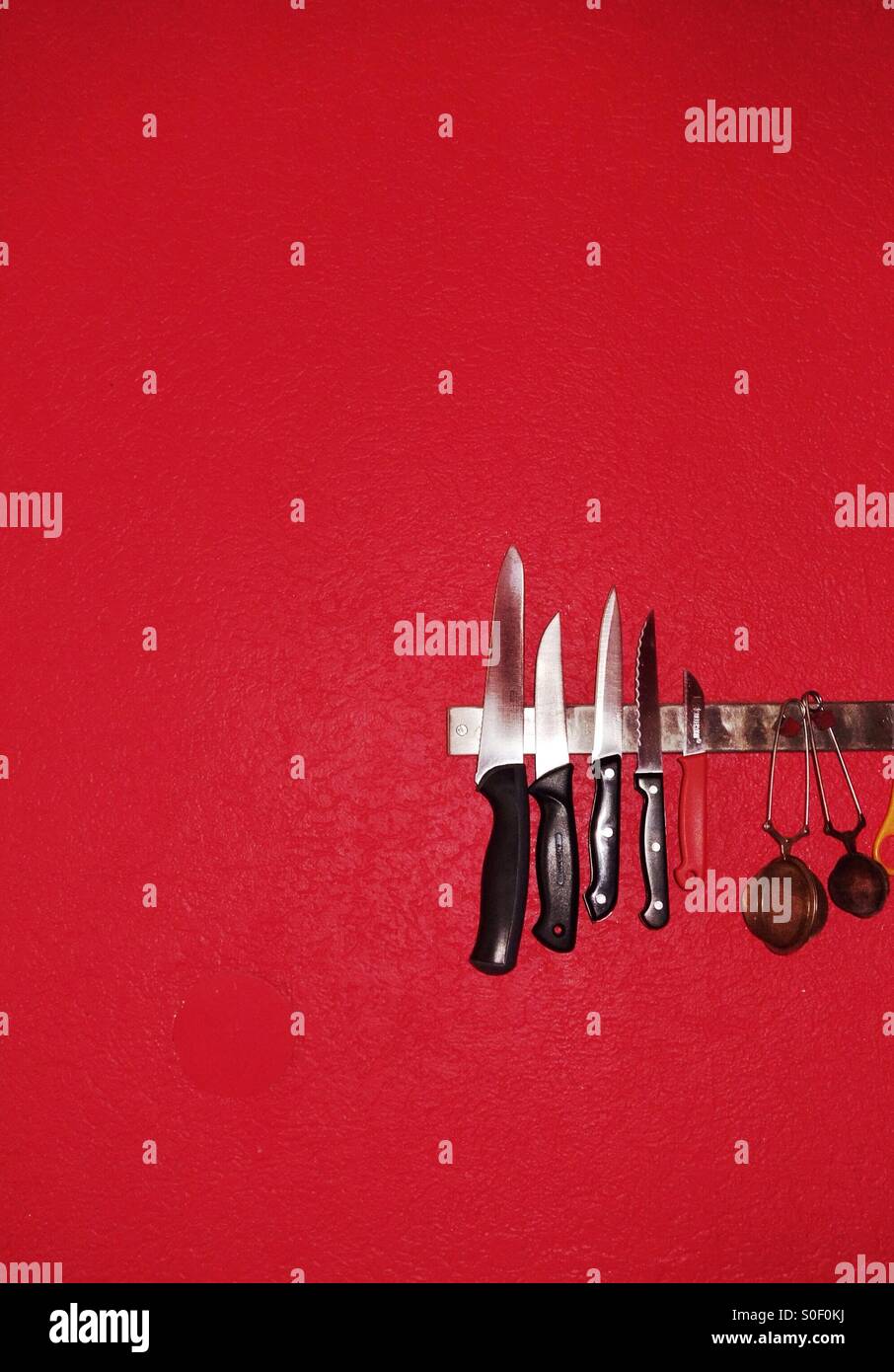 Kitchen knives on a magnetic holder against a bright red wall Stock Photo