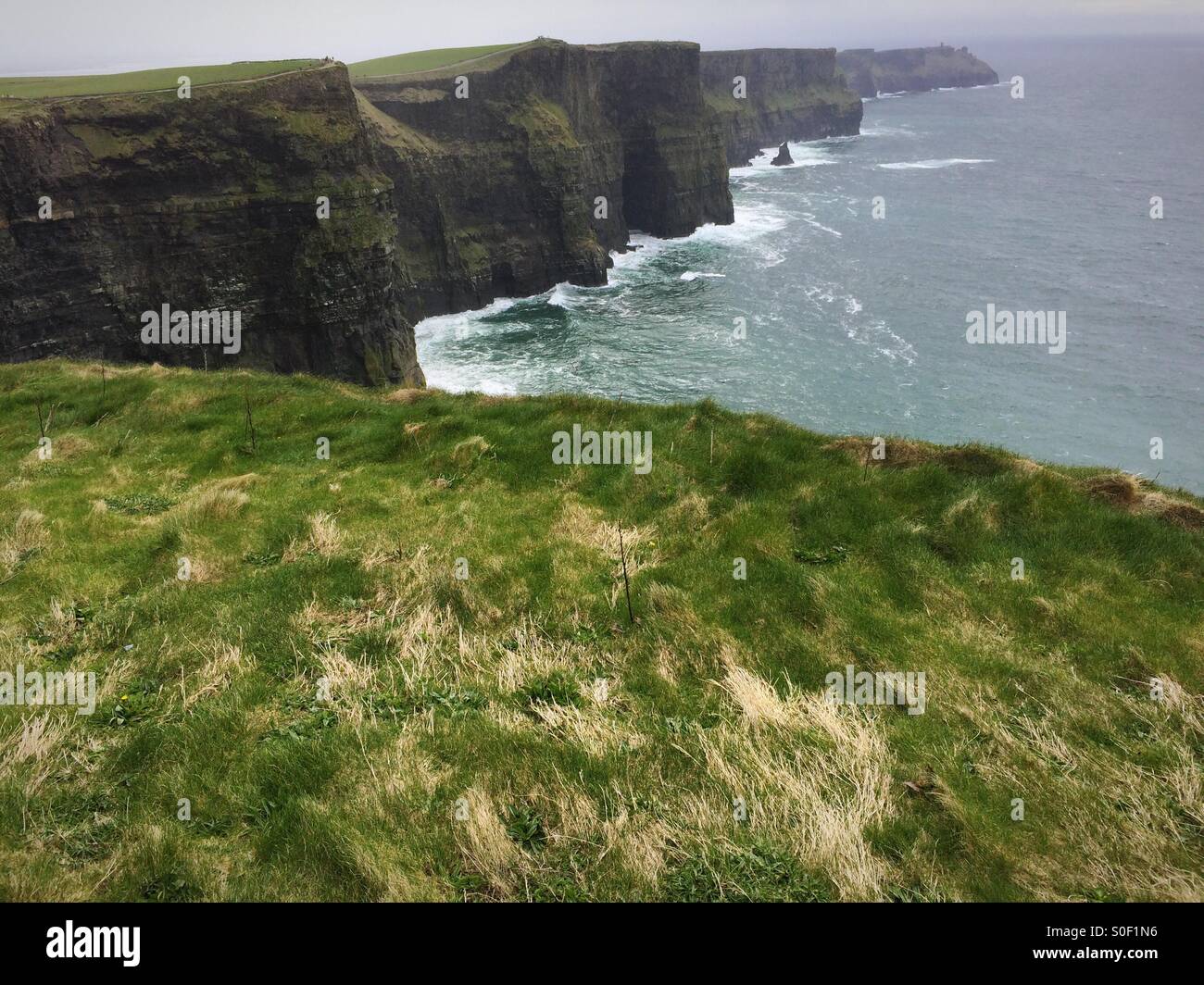 Cliffs of Moher Ireland. Dramatic view of rocks and sea with green grass in the foreground. - Smartphone Captured Stock Image
