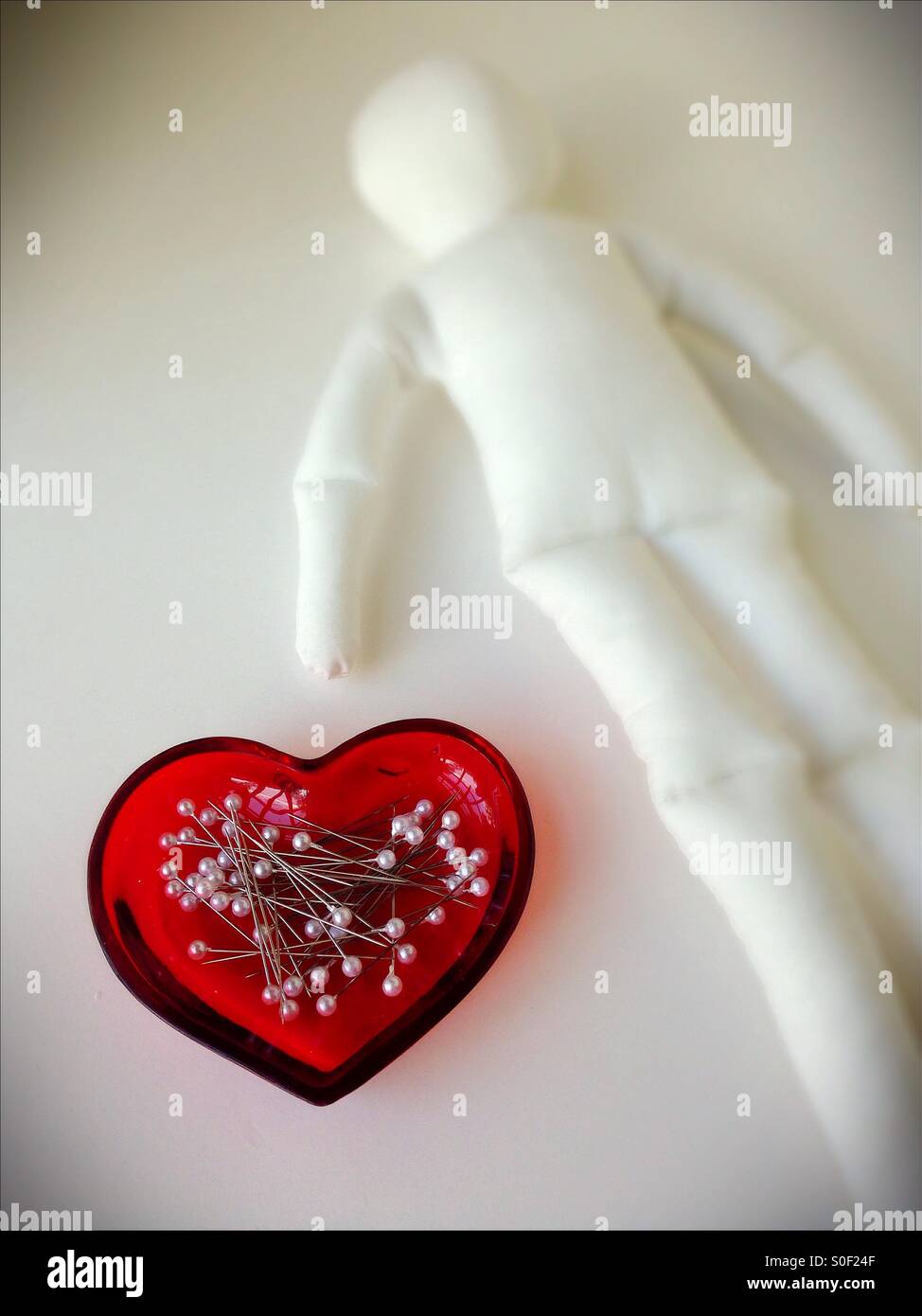 Pins in a heart shaped dish next to a blank voodoo doll. Stock Photo