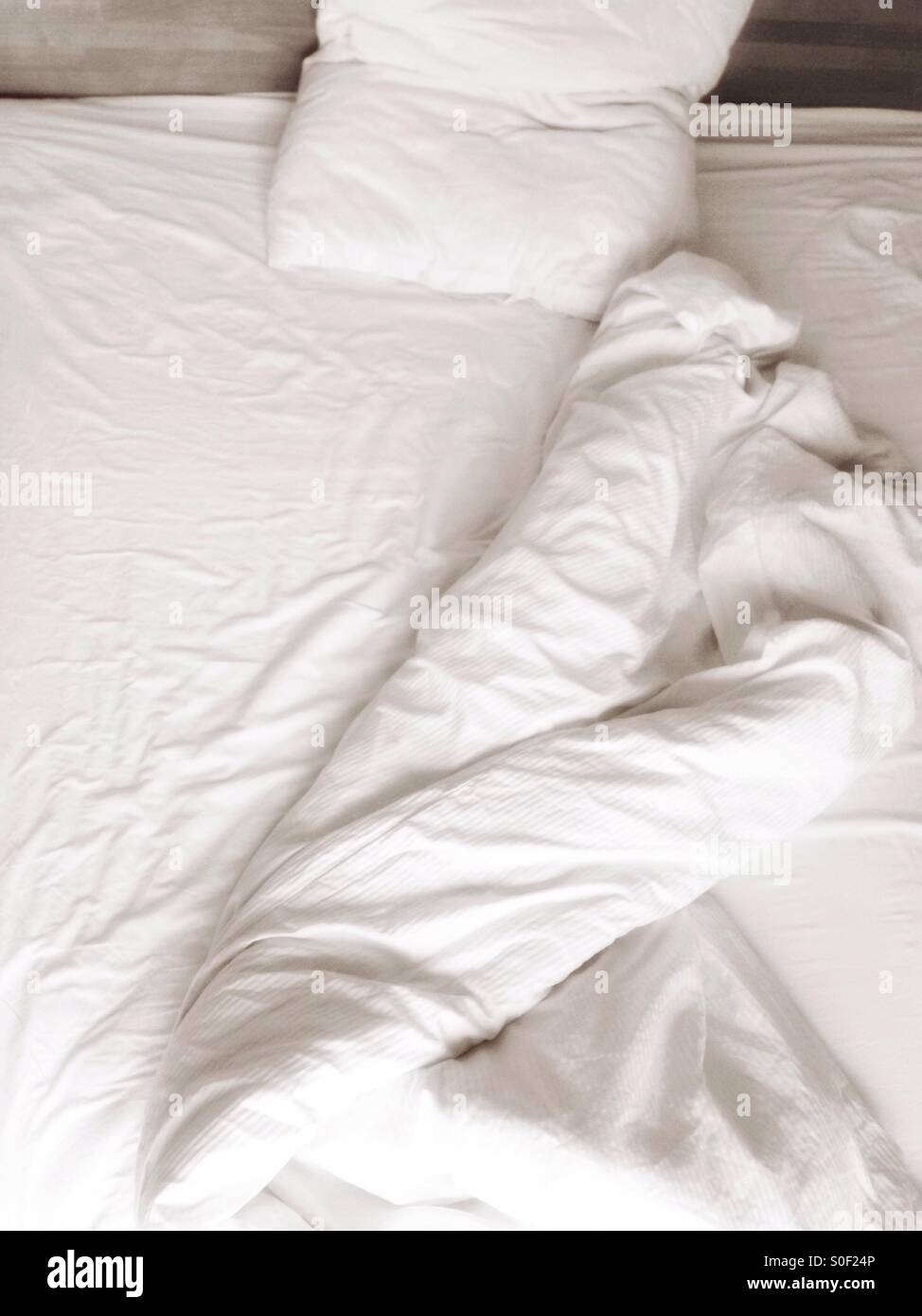 An unmade bed with white linen Stock Photo