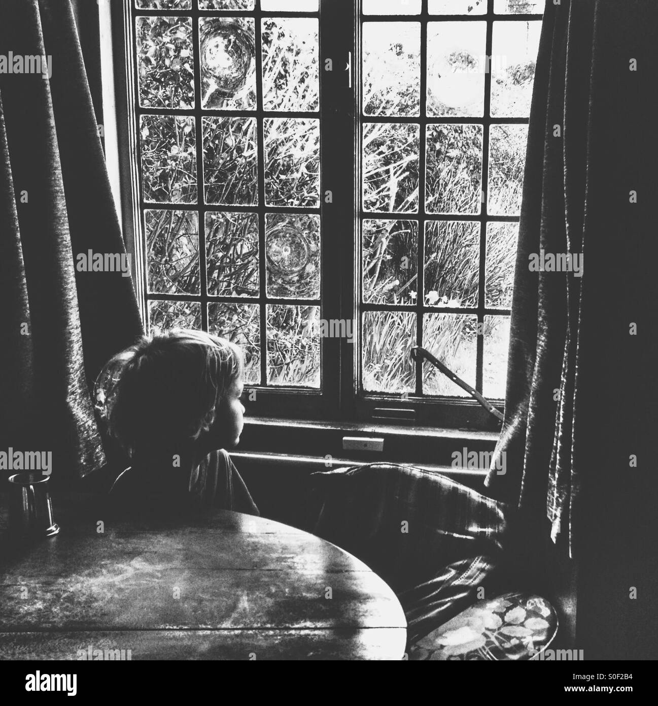 Child sat at table gazing out of window - Smartphone Captured Stock Image