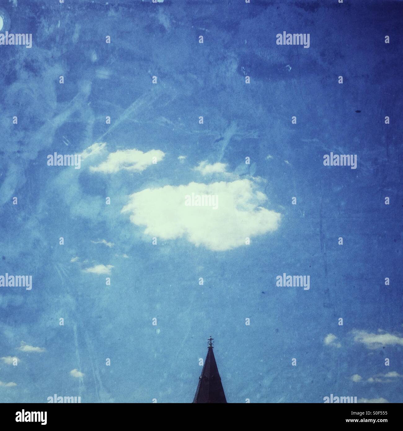A Fluffy white Cloud in a Blue Sky above a pointy church Tower - Smartphone Captured Stock Image