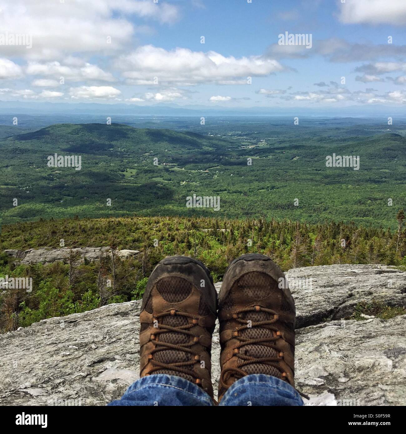 Feet in Hiking boots on a stone overlook looking towards the Champlain Valley and Lake Champlain from Mount Mansfield in Underhill, Vermont Stock Photo