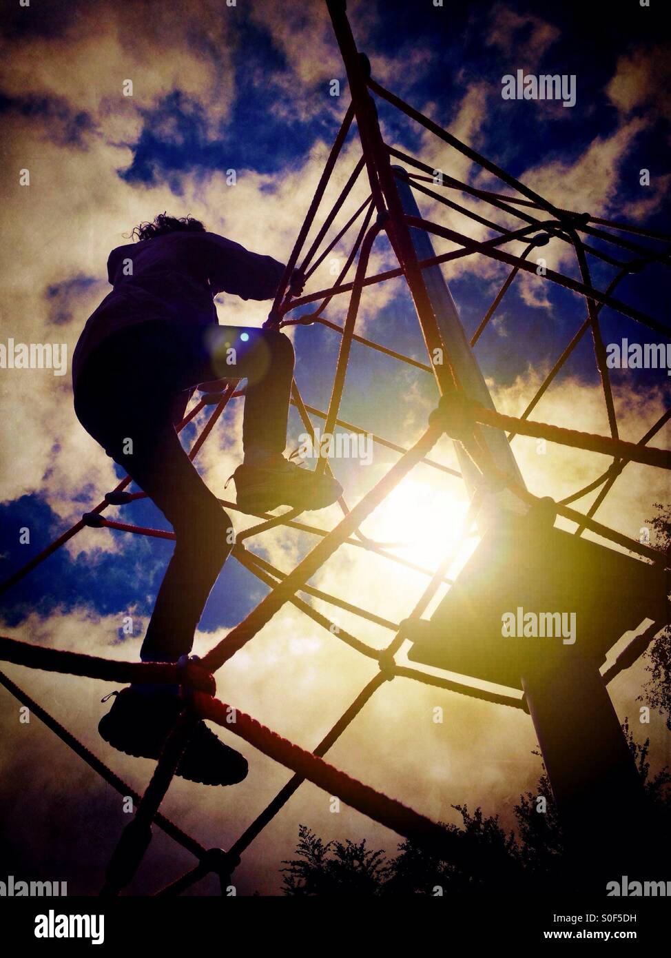 Young girl climbing rope climbing frame looking into sun Stock Photo ...