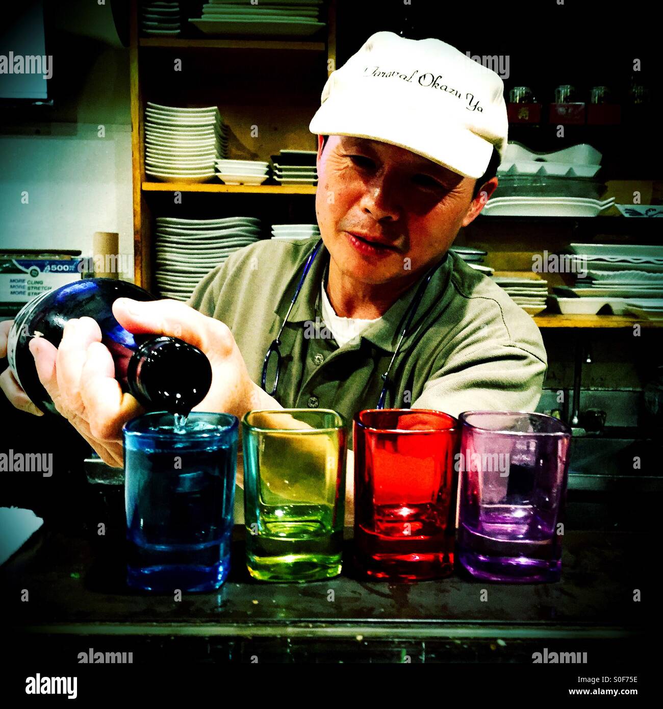 Sushi master pours four brightly colored cups of premium cold sake for his favorite customers. - Smartphone Captured Stock Image