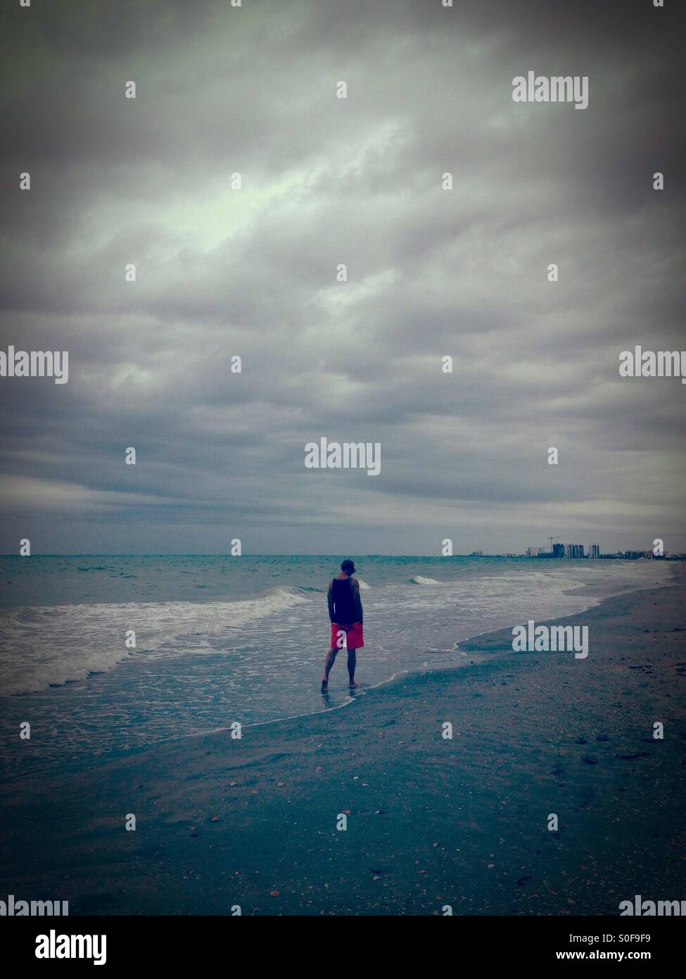 Man walking on beach under a stormy sky - Smartphone Captured Stock Image