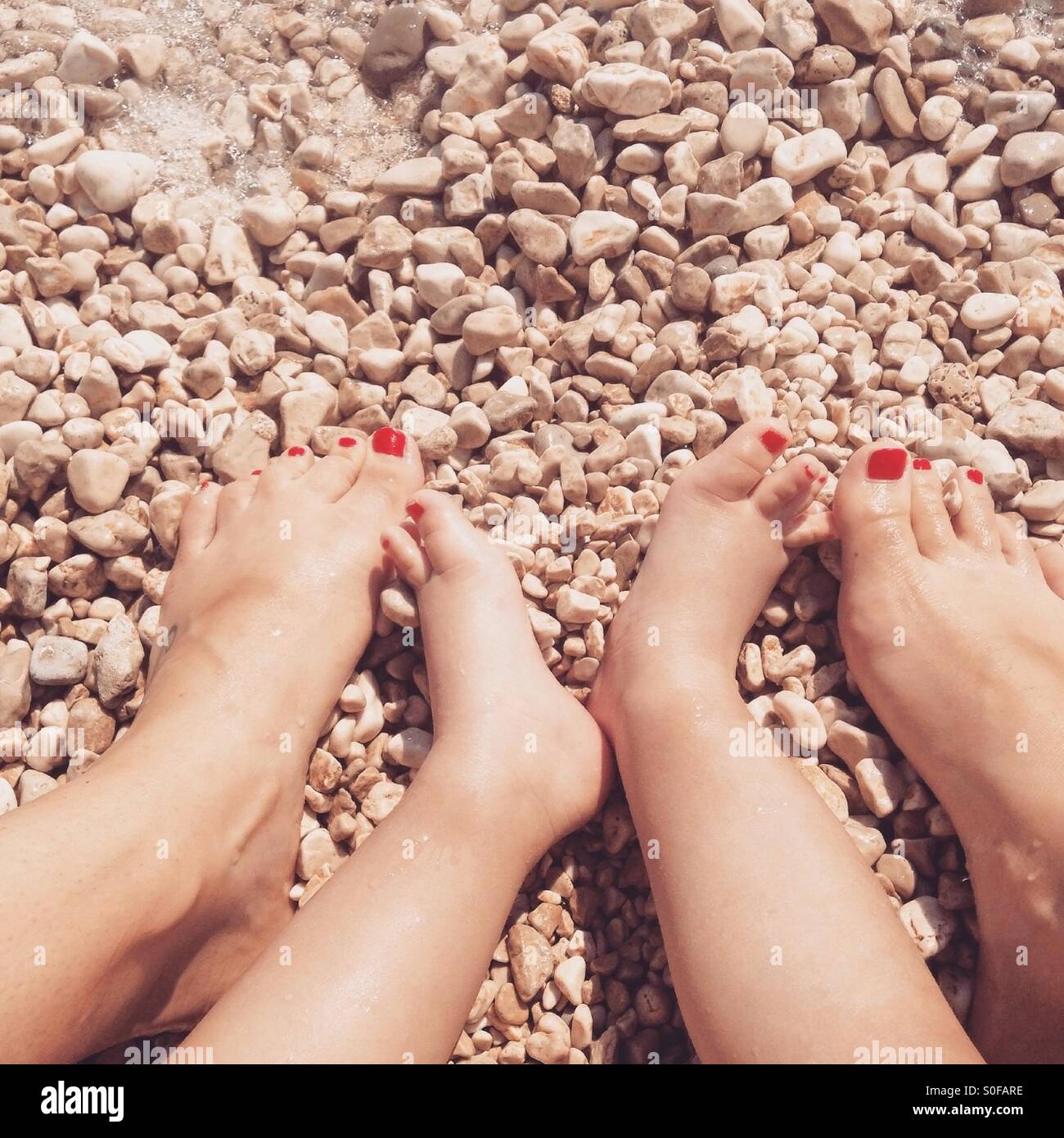 Mom and daughter legs with red nailed fingers on beach Stock Photo