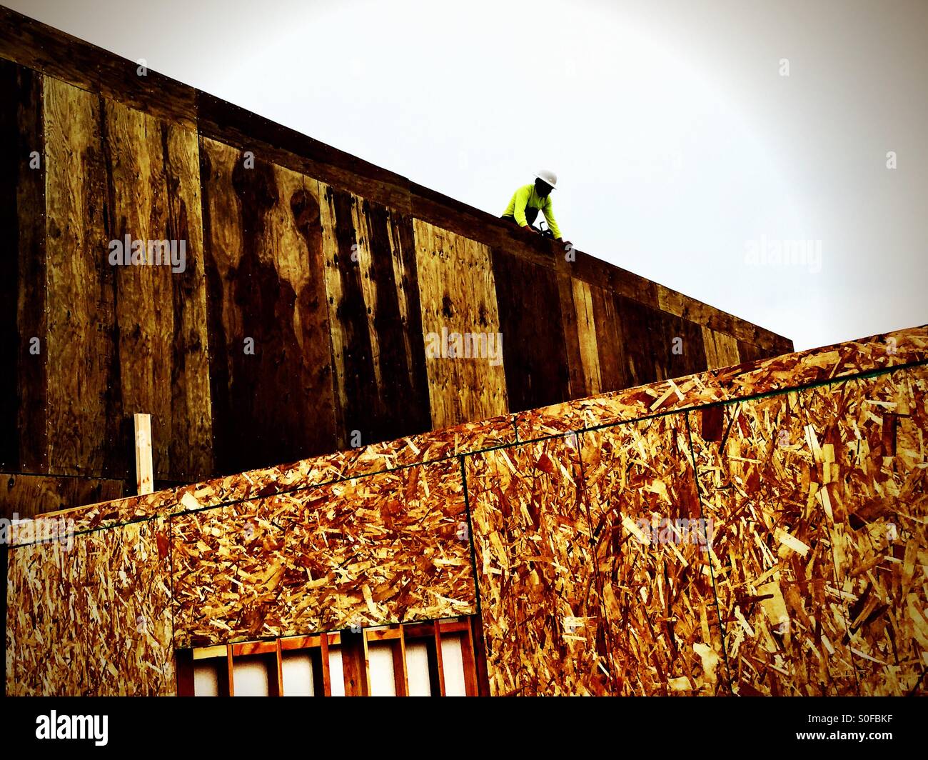 Helmet clad worker in safety green atop near completed frame for new condominium project. Orthographic geometry, San Francisco, California, USA. - Smartphone Captured Stock Image