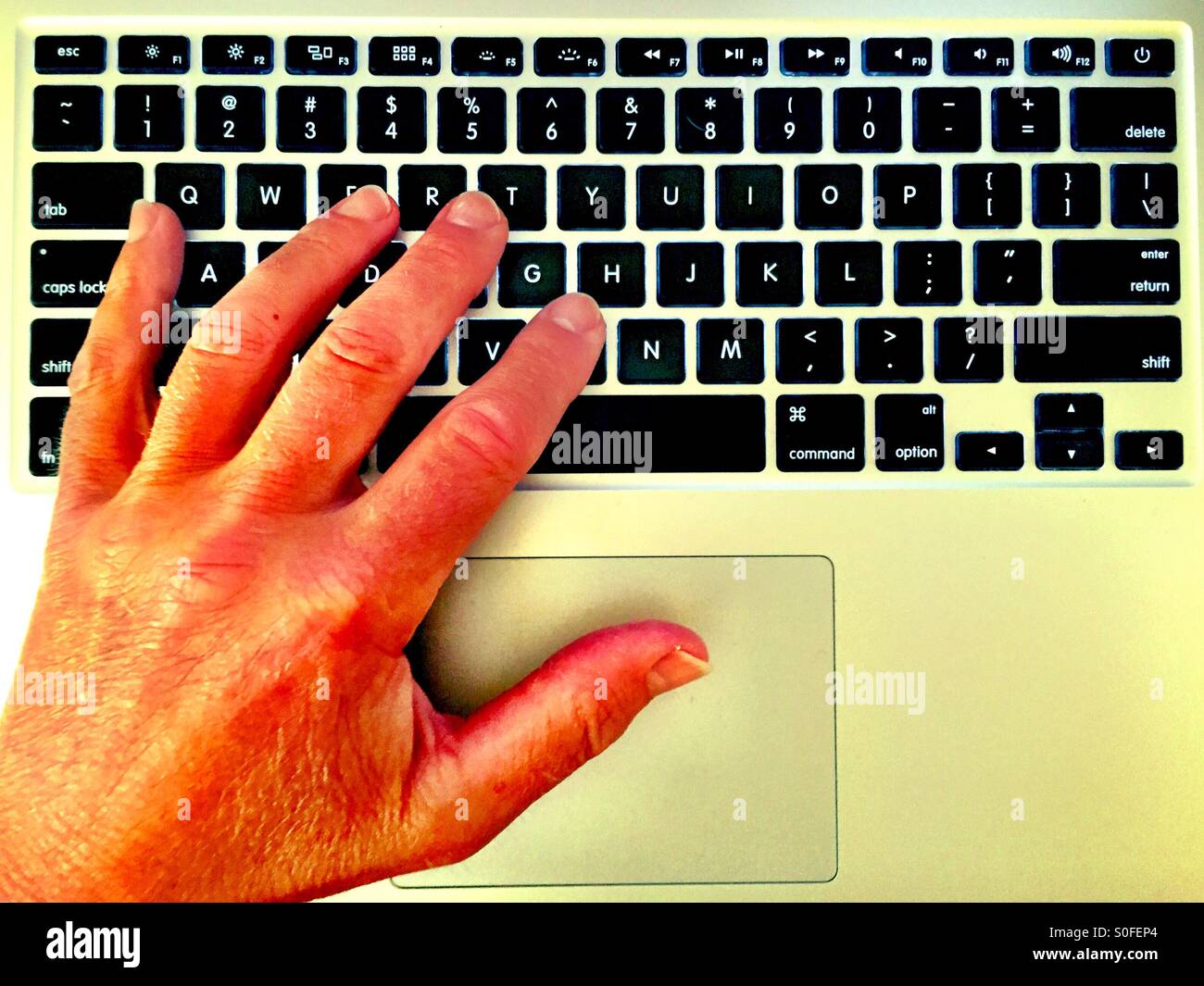 Sunlit man's left hand reaching for keyboard on laptop computer. - Smartphone Captured Stock Image