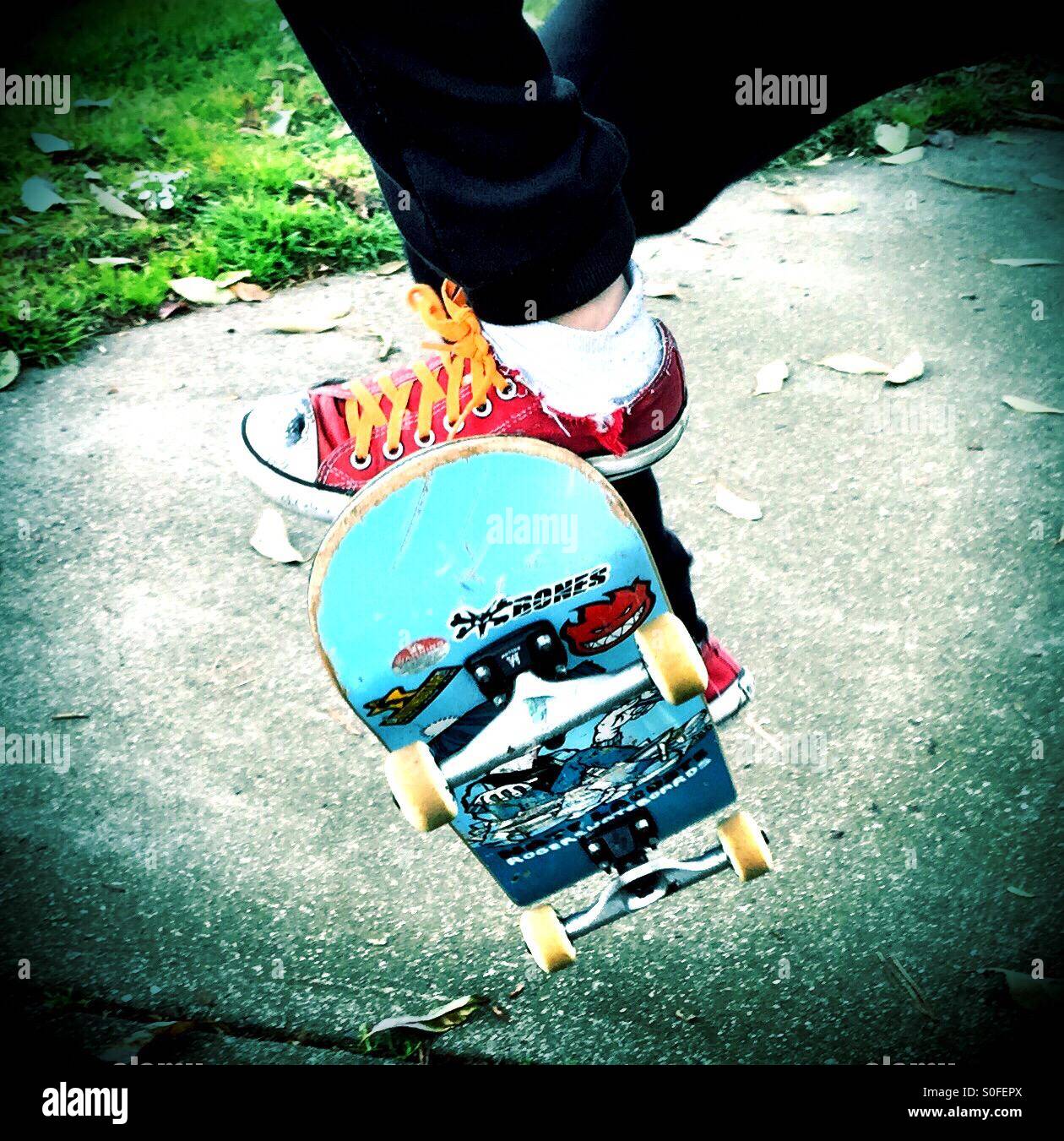 Clad in red sneakers and orange shoelaces, youth kicks up and gets air with skateboard over the sidewalk. - Smartphone Captured Stock Image
