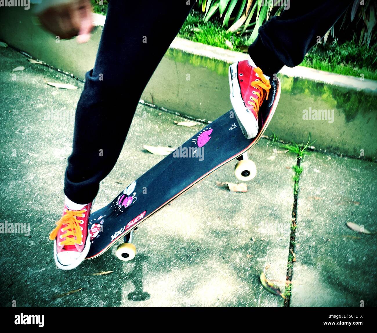 Kicking up skateboard over a sidewalk. Red sneakers, urban youth. - Smartphone Captured Stock Image
