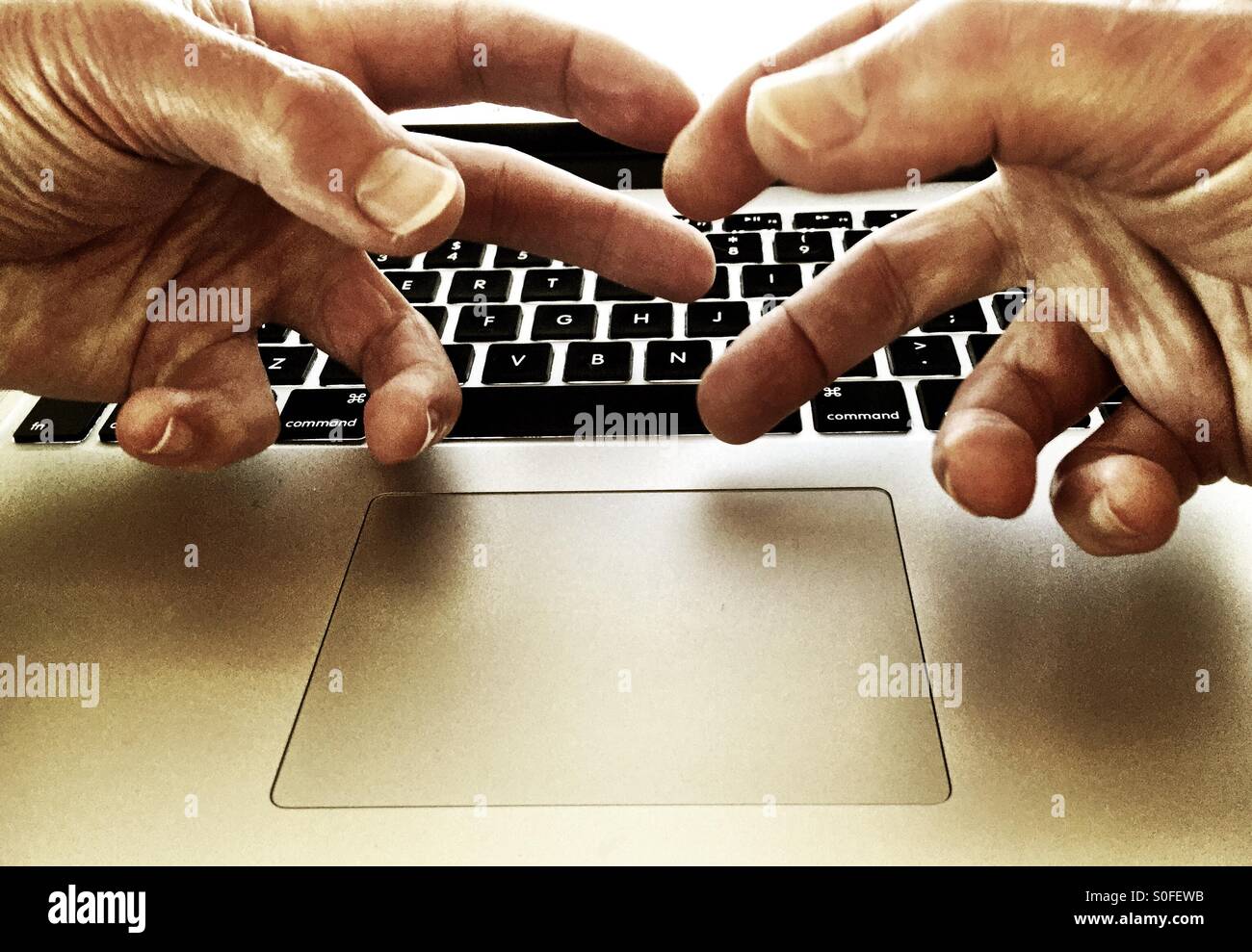 Frustrated gnarled fingers over laptop computer keyboard. Sepia tone. Stock Photo