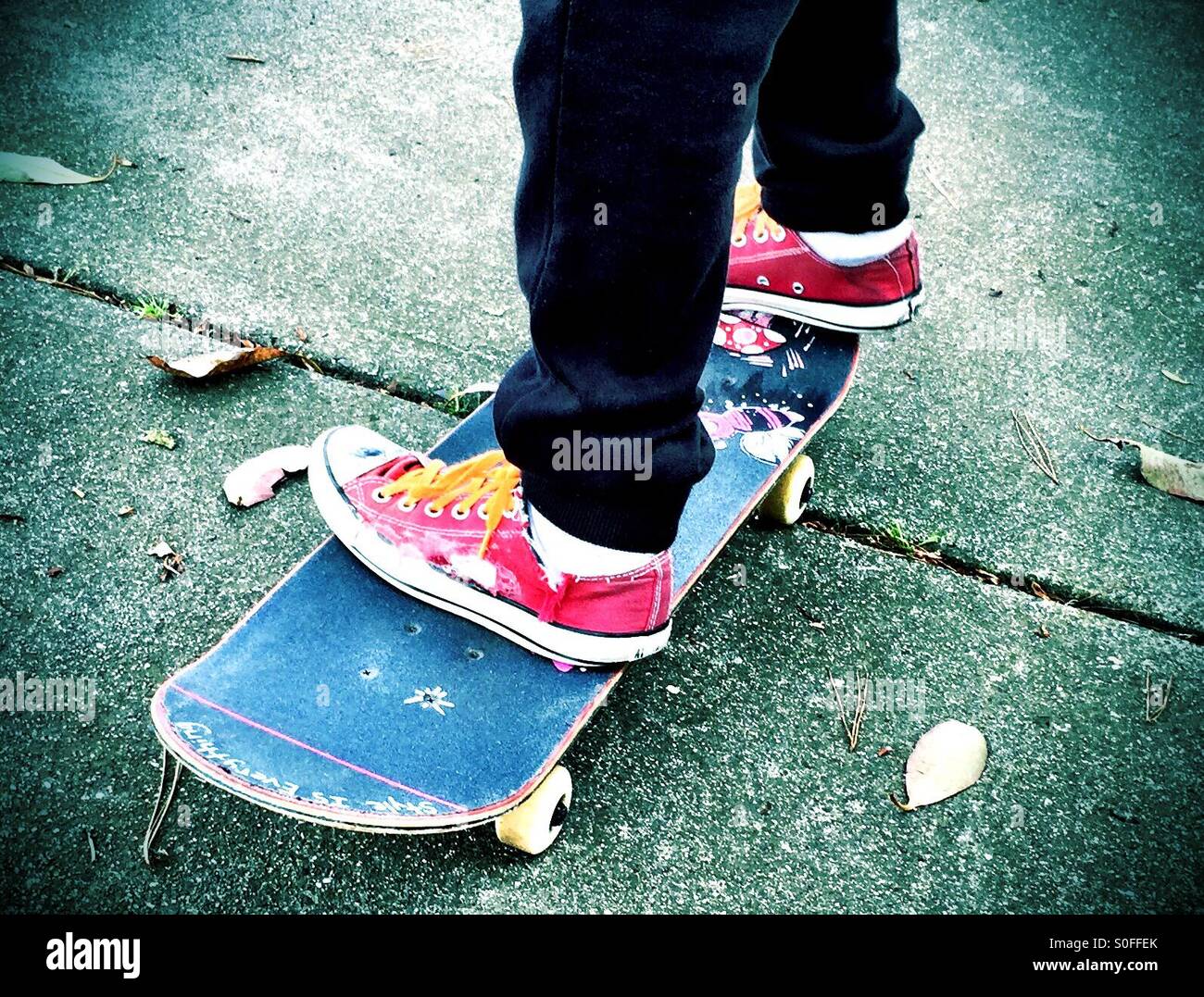 Youth in red sneakers and orange shoelaces travels down urban sidewalk on blue skateboard. - Smartphone Captured Stock Image
