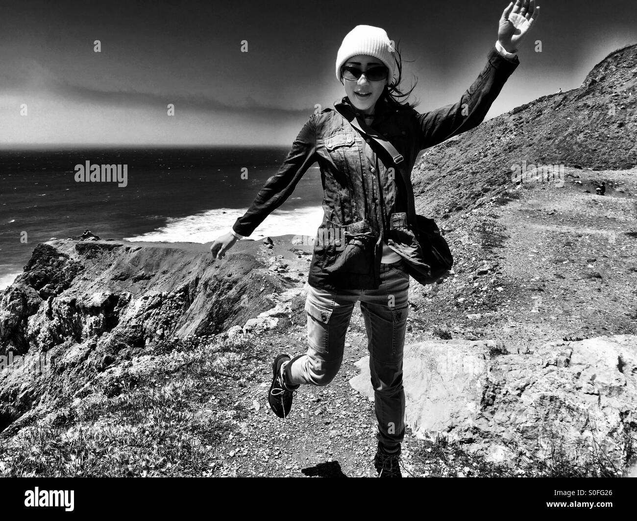 Young woman flies through the cool air along the coastal cliffs in Pacifica, California, USA. Black and white, film noir. Suspended animation. Stock Photo
