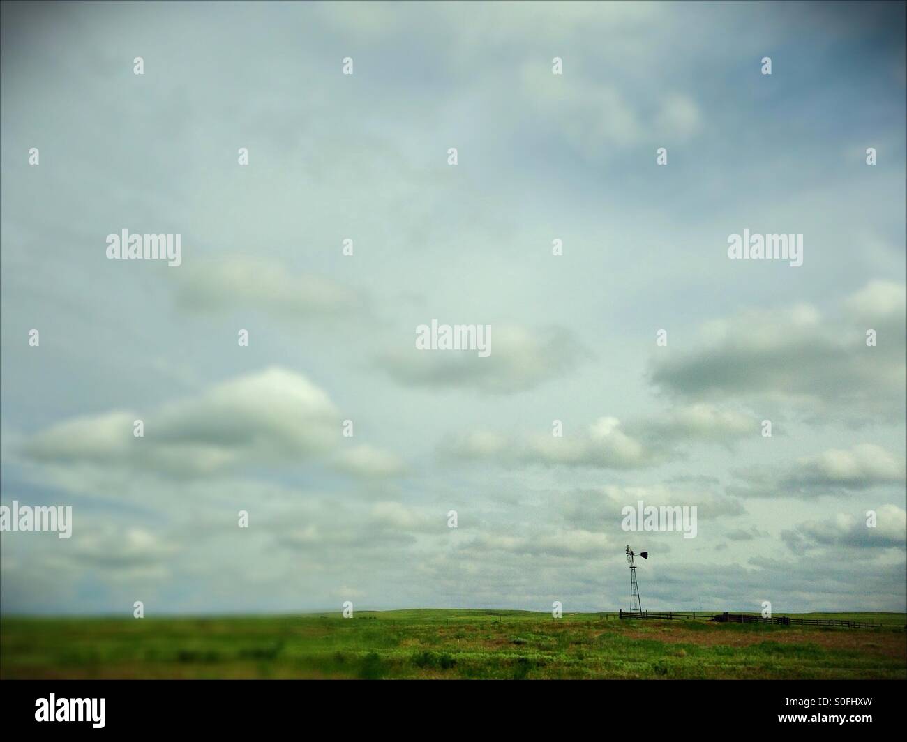 A windmill under puffy clouds in a field in Nebraska. Stock Photo