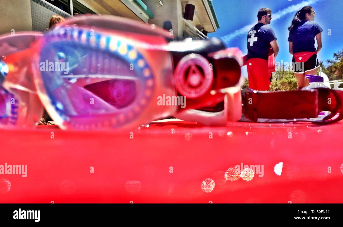 View of lifeguards on deck as seen from a swimmer in the pool, past swim goggles on a kickboard. - Smartphone Captured Stock Image