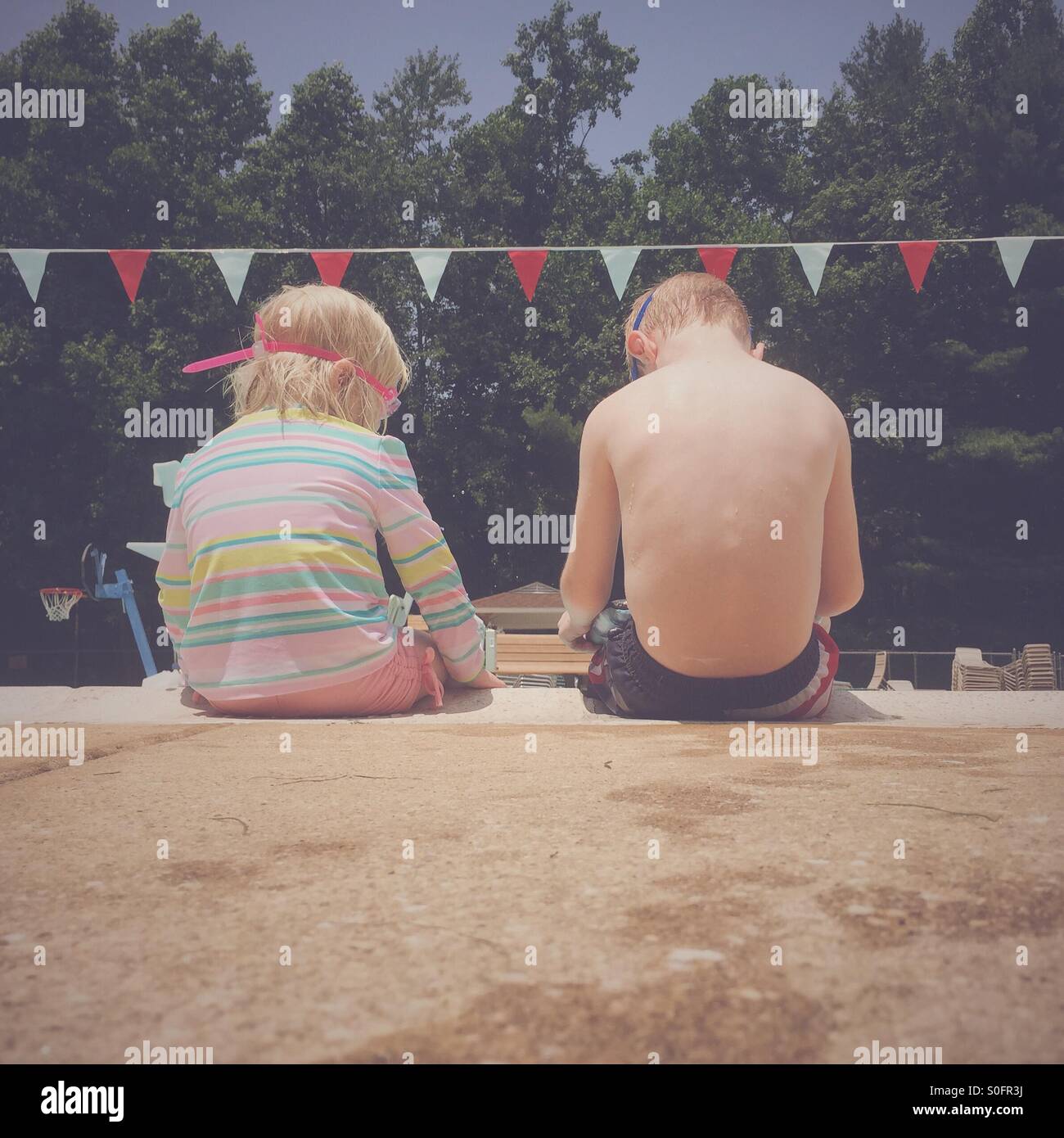 Two young children sitting next to each other on the side of a swimming pool. Stock Photo