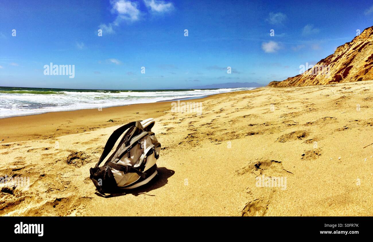 Lone backpack lying on a long empty stretch of sunny inviting California beach in June. Stock Photo