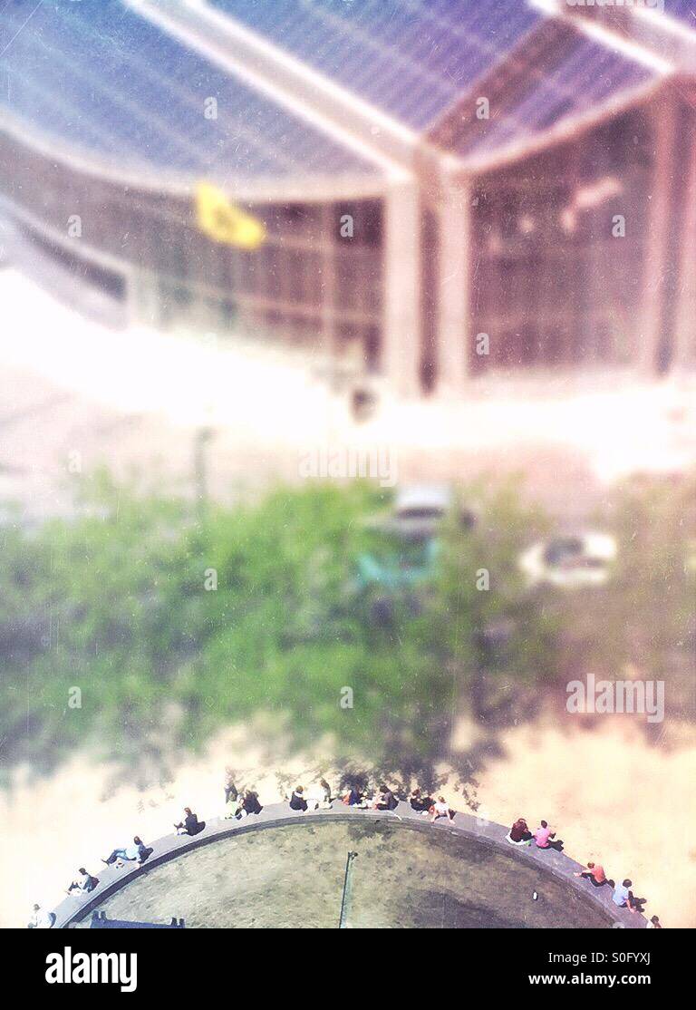 People sitting on the border of a rounded fountain in front of a round office building - Smartphone Captured Stock Image