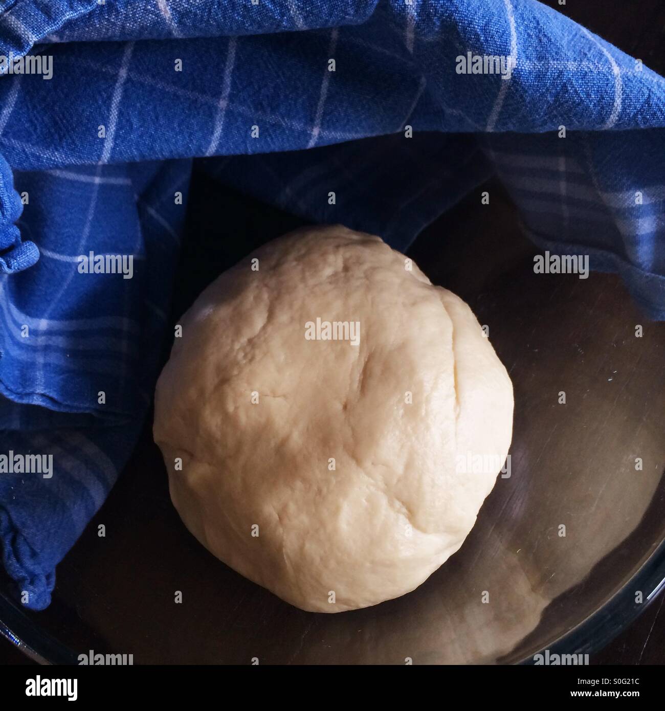 Bread dough proofing in glass bowl with blue kitchen towel Stock Photo