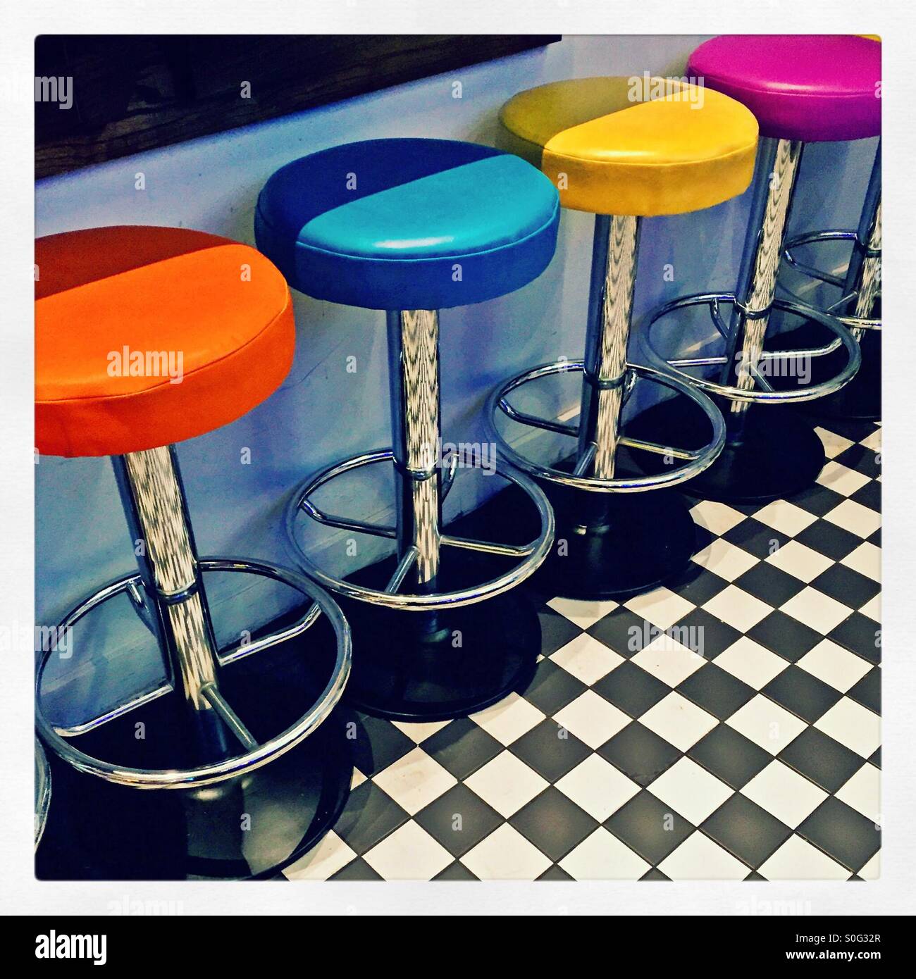 Brightly coloured bar stools on a chequered floor Stock Photo - Alamy