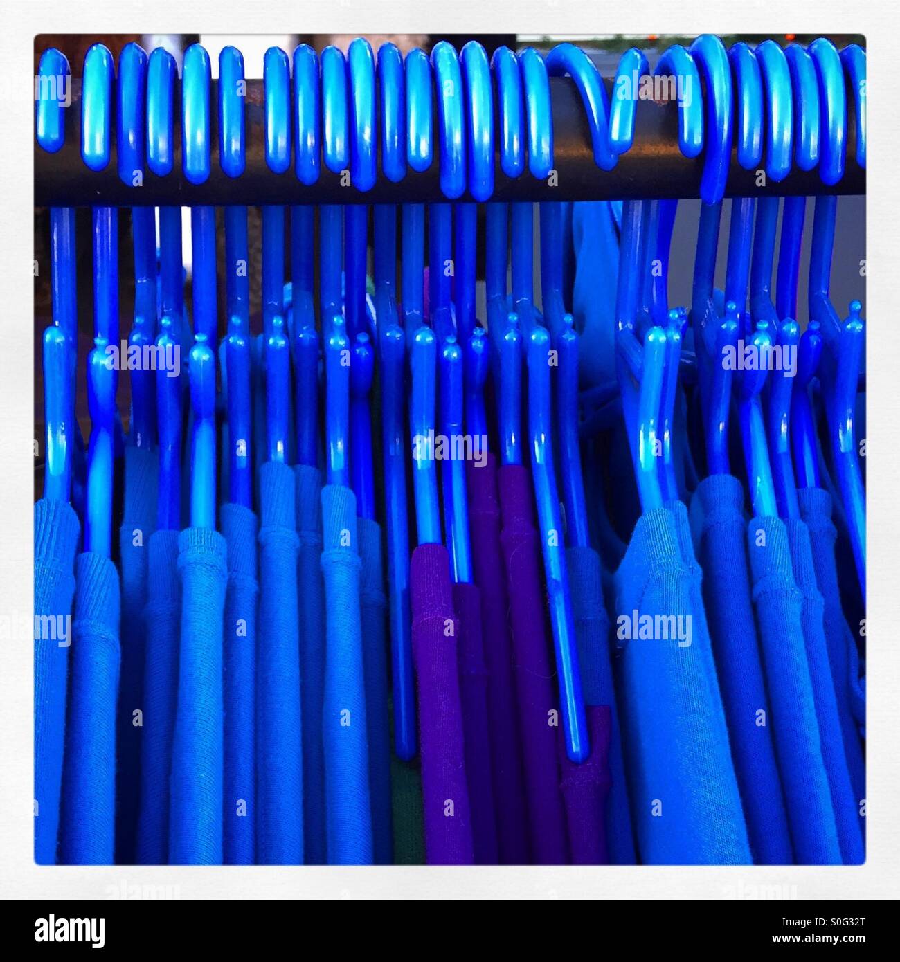 A rack of blue plastic hangers with blue garments Stock Photo