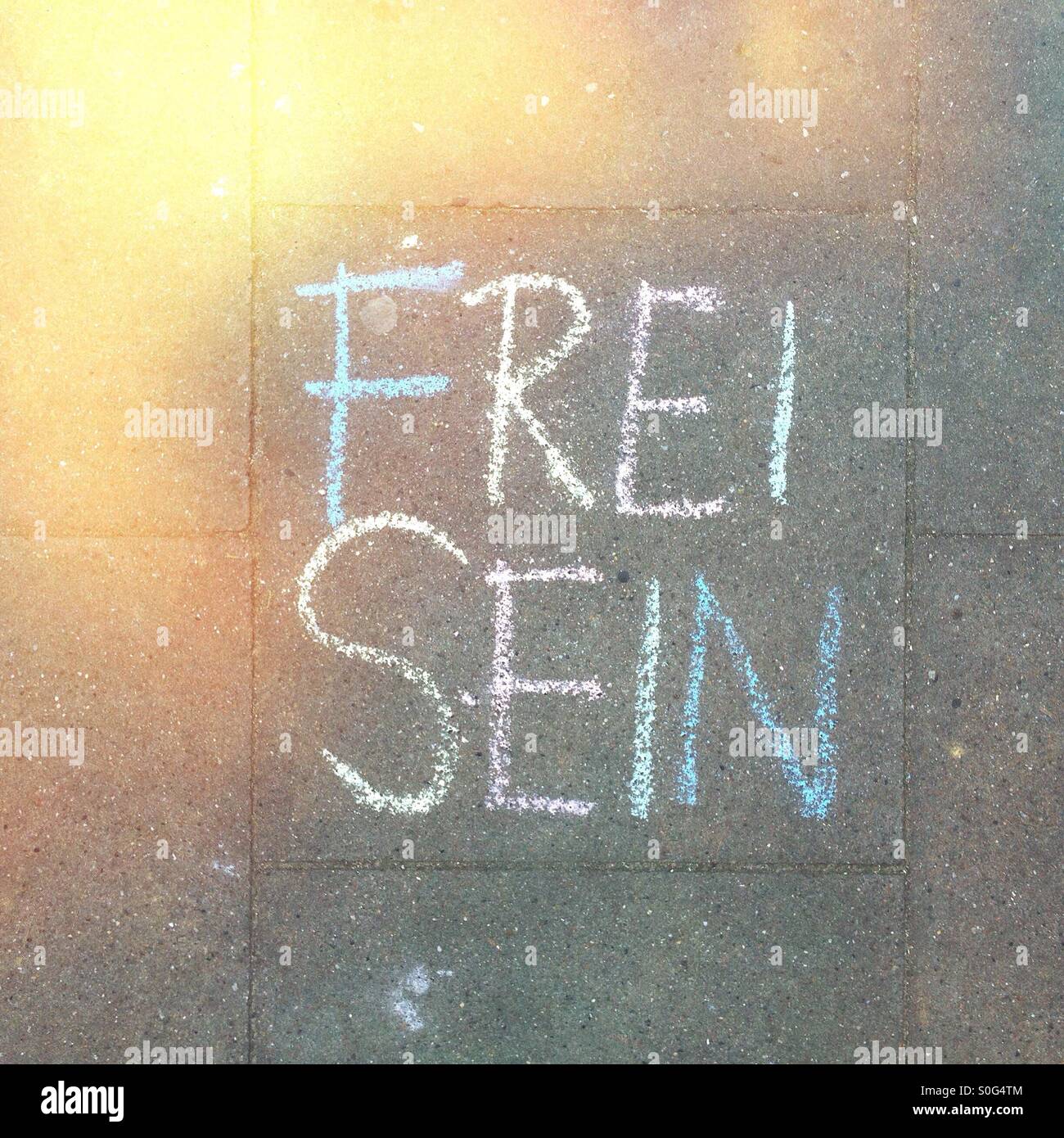 The words 'Frei Sein' (Be Free) written on the sidewalk in German with colorful chalk Stock Photo