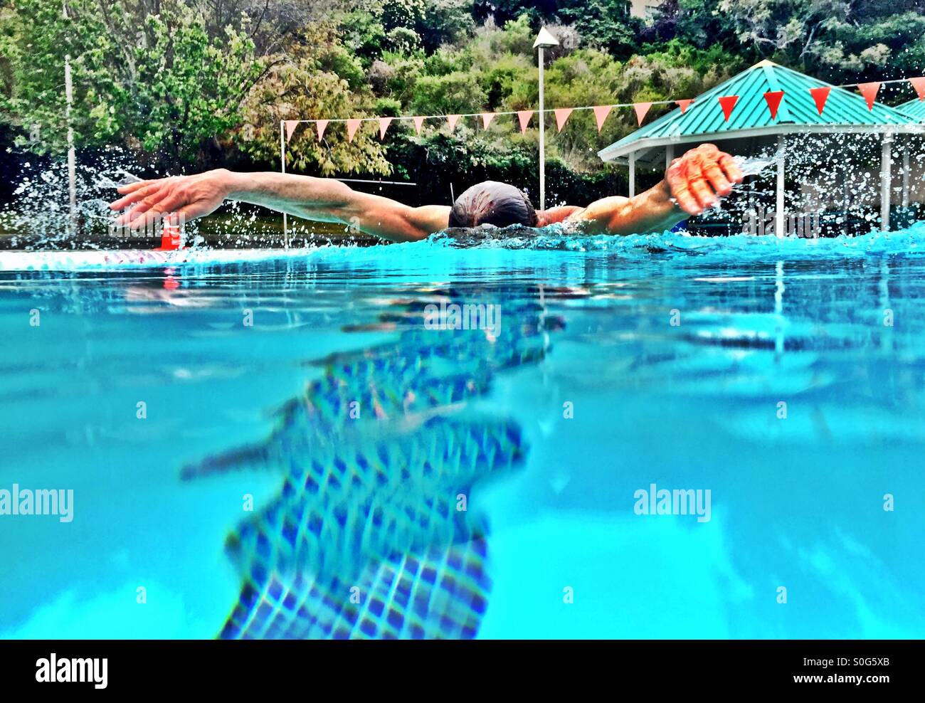 Closeup from middle of the lane, athlete swims butterfly stroke, radiating water droplets to complete the metamorphosis. - Smartphone Captured Stock Image