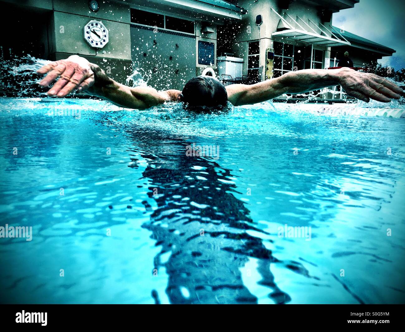 Swimming butterfly stroke, an athletic male swimmer. Closeup, inches-away action view from inside the same lane. - Smartphone Captured Stock Image