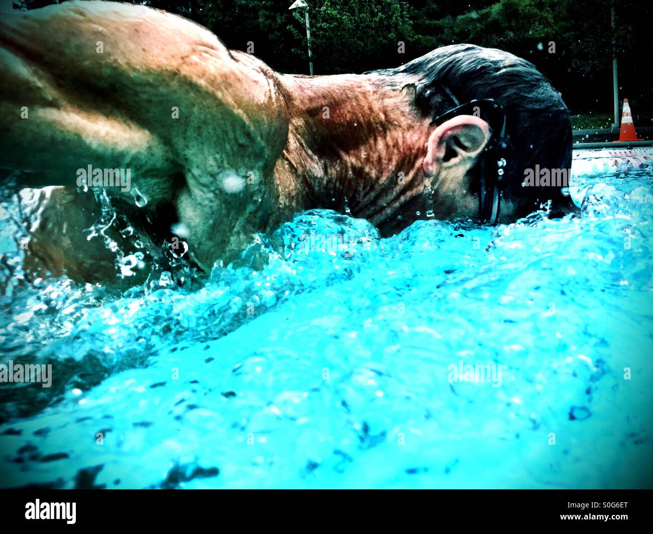 Extreme closeup of muscular swimmer mid butterfly stroke in an outdoor swimming pool. - Smartphone Captured Stock Image
