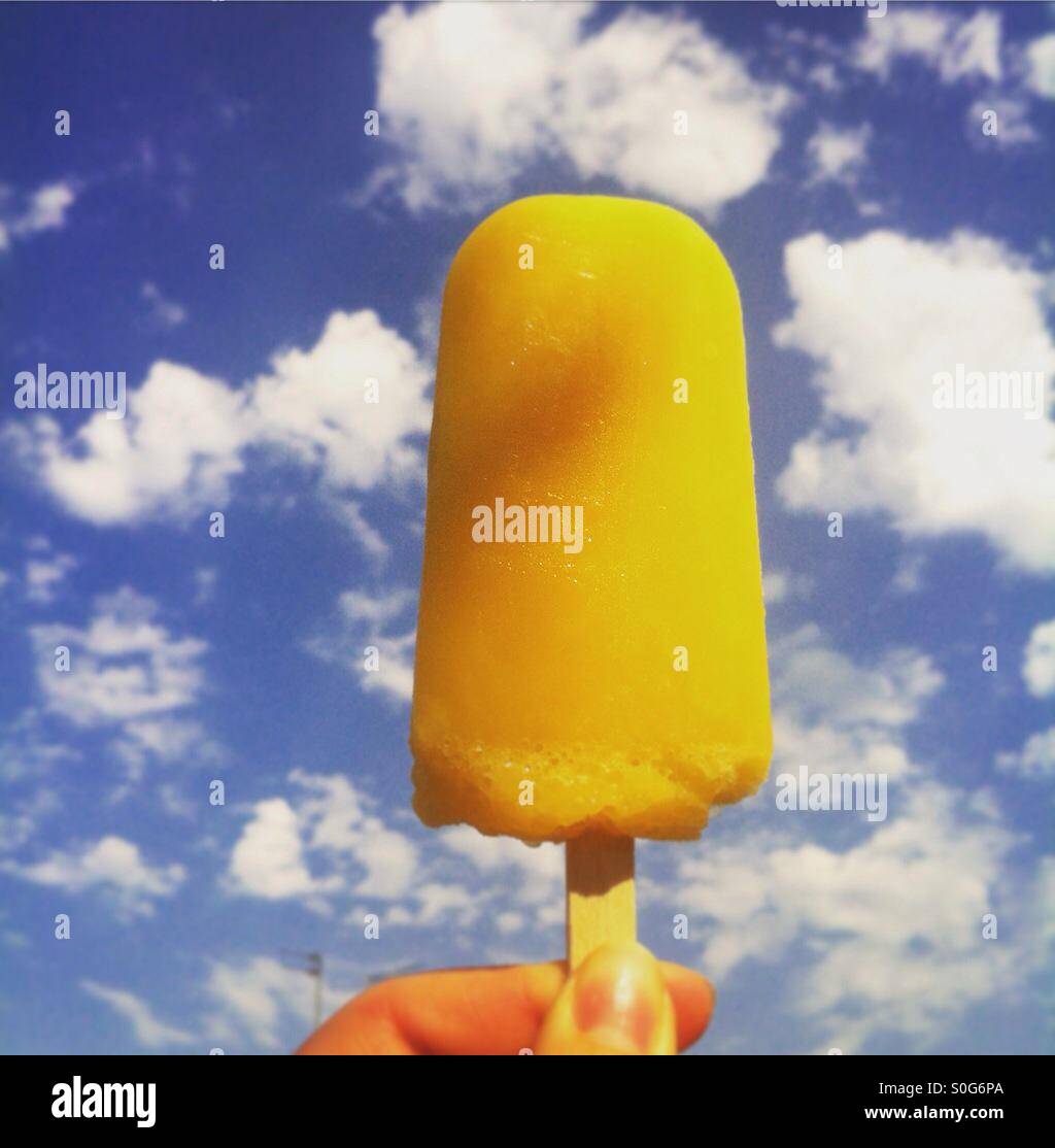Orange ice-lolly on a background of deep blue sky with fluffy white clouds Stock Photo