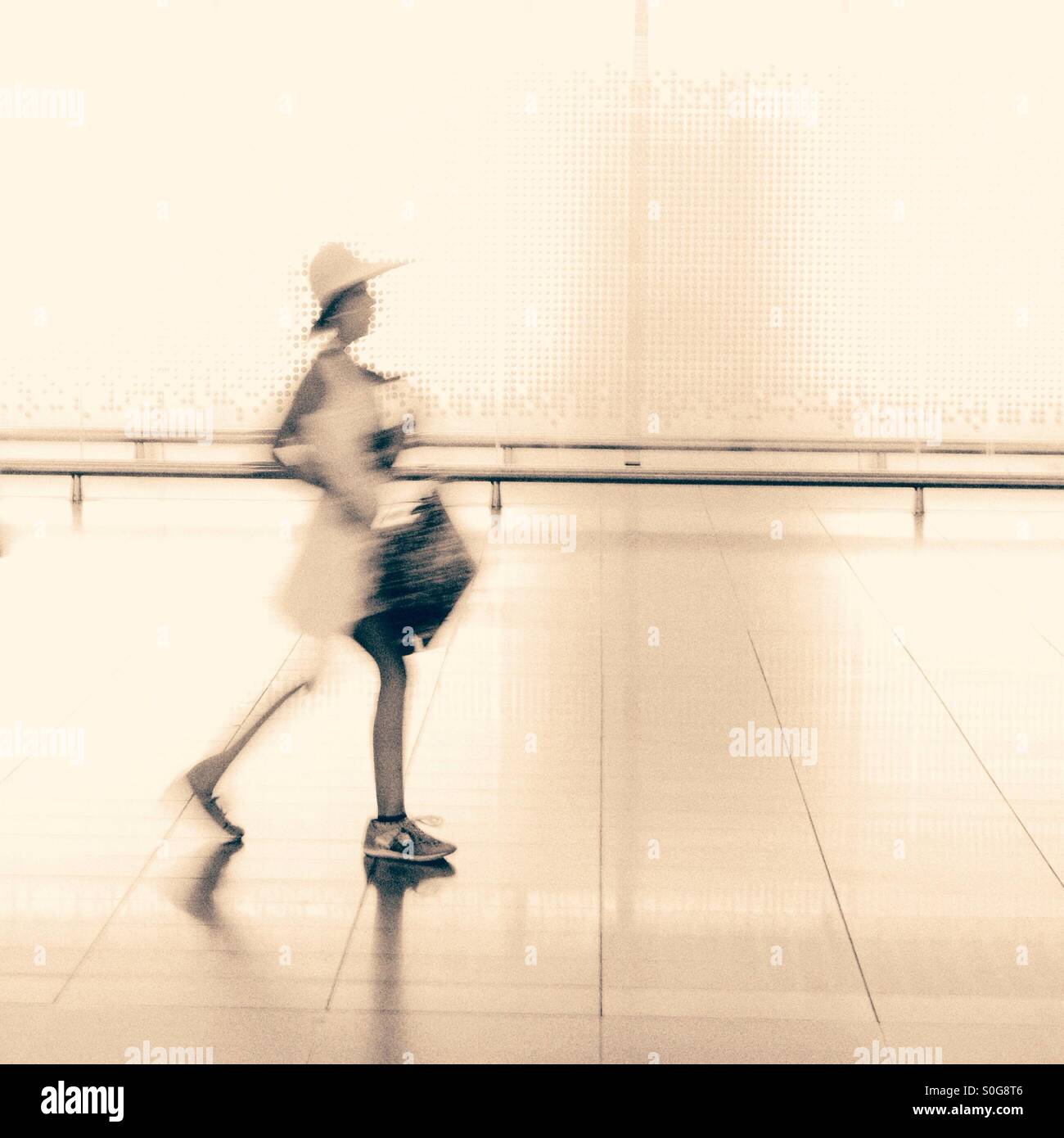 A blurred figure wearing a hat walking with bags - Smartphone Captured Stock Image