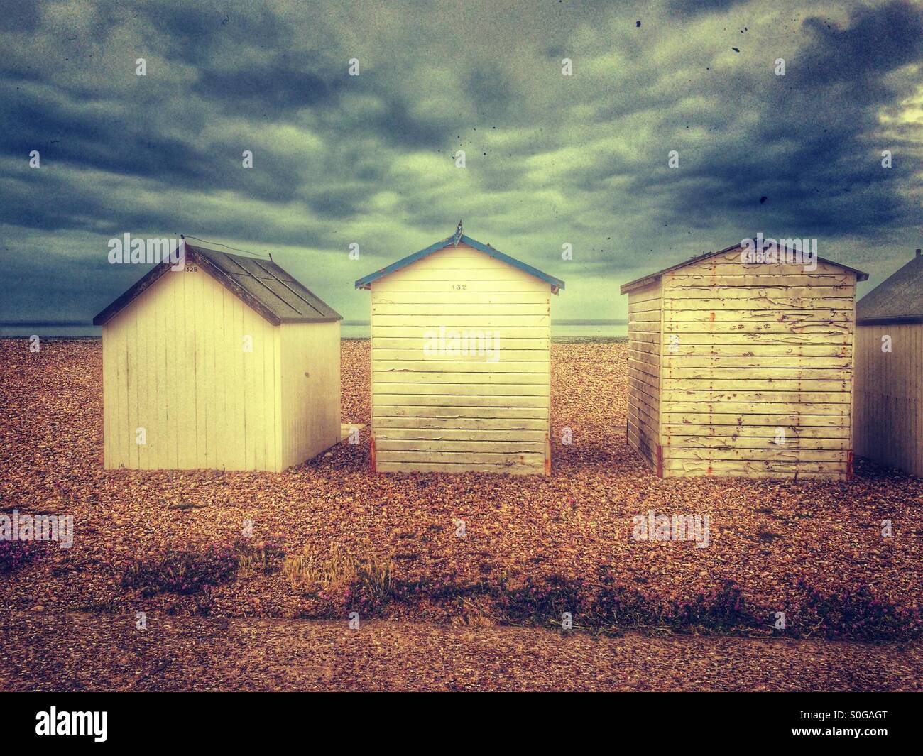 Three painted wooden beach huts on a shingle beach in goring by sea