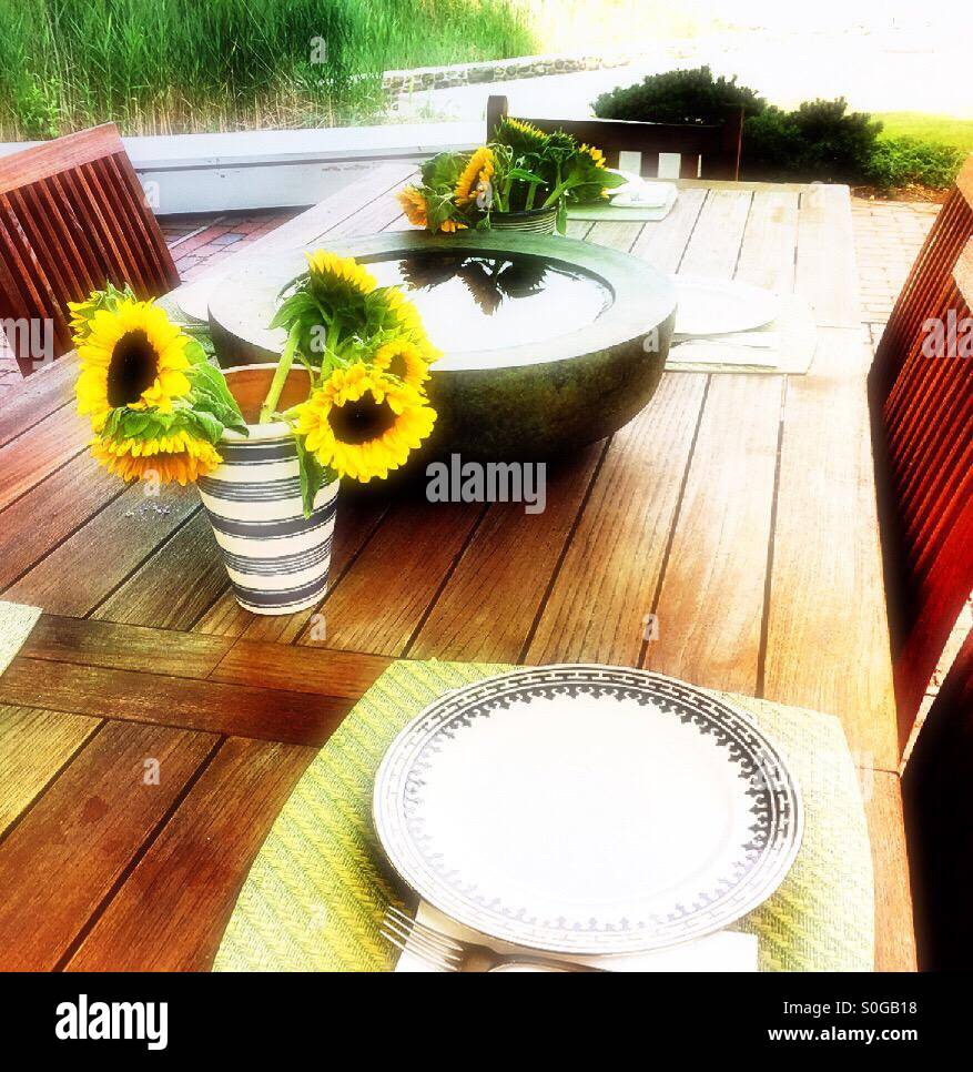 Decorative water cistern and sunflowers on long wooden table on outdoor patio, USA - Smartphone Captured Stock Image