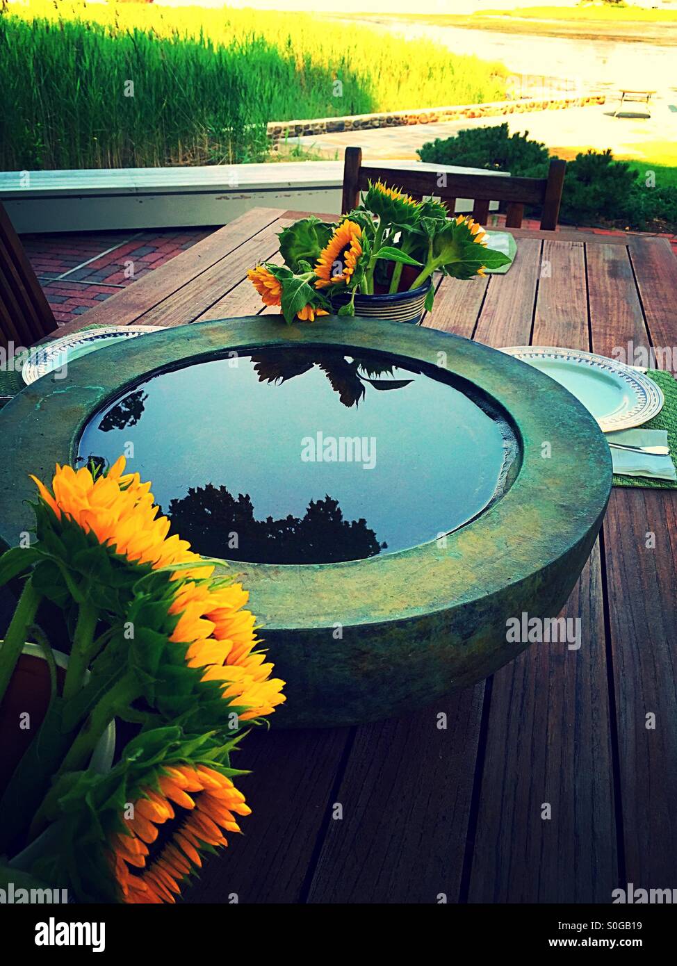 Decorative water system cistern and sunflowers on outside patio table, USA - Smartphone Captured Stock Image