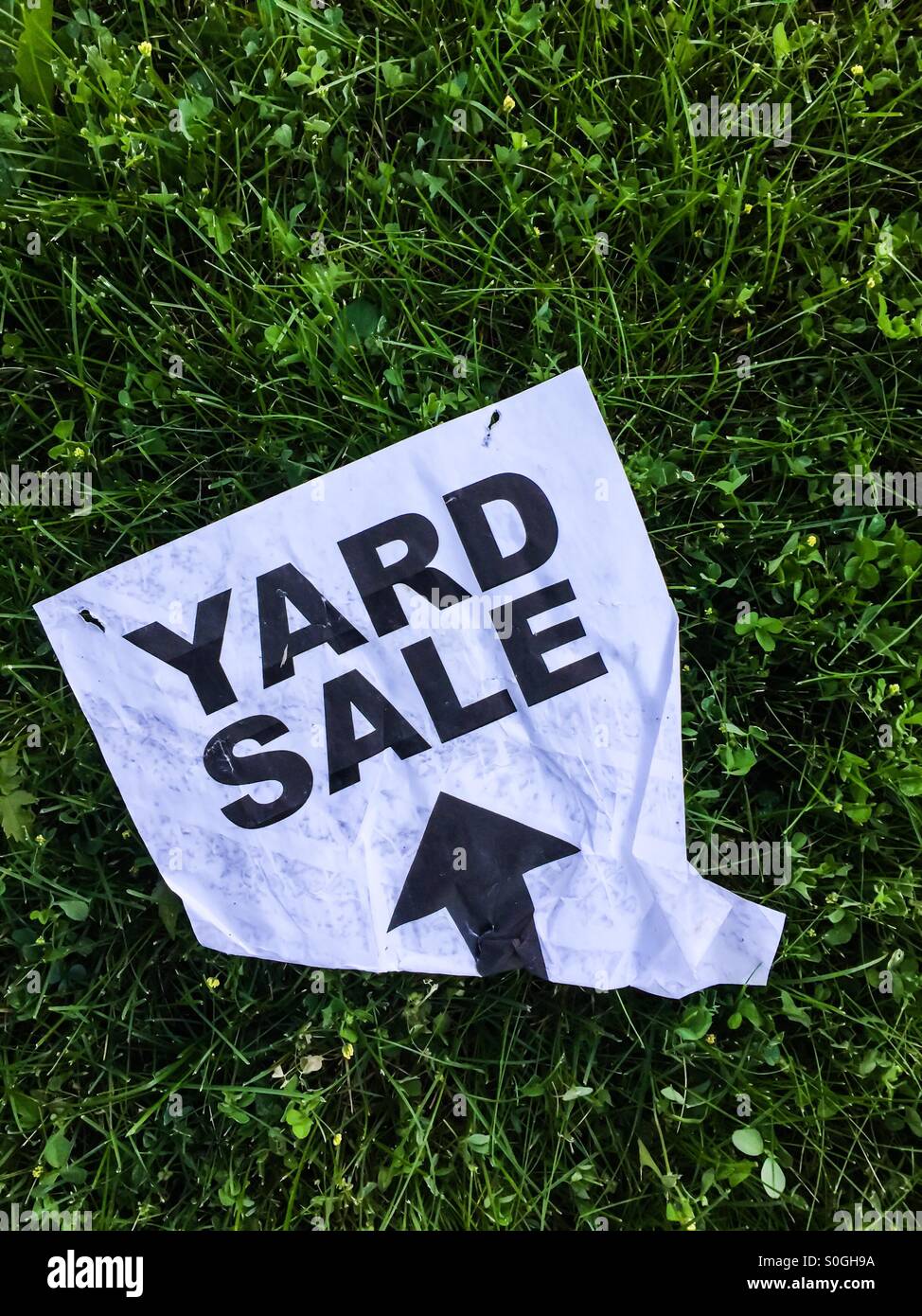 Yard sale. A sign with a directional arrow on the ground. Maybe discarded the day after. Bold type. Black and white. Plain and simple. On green grass. Canada. - Smartphone Captured Stock Image